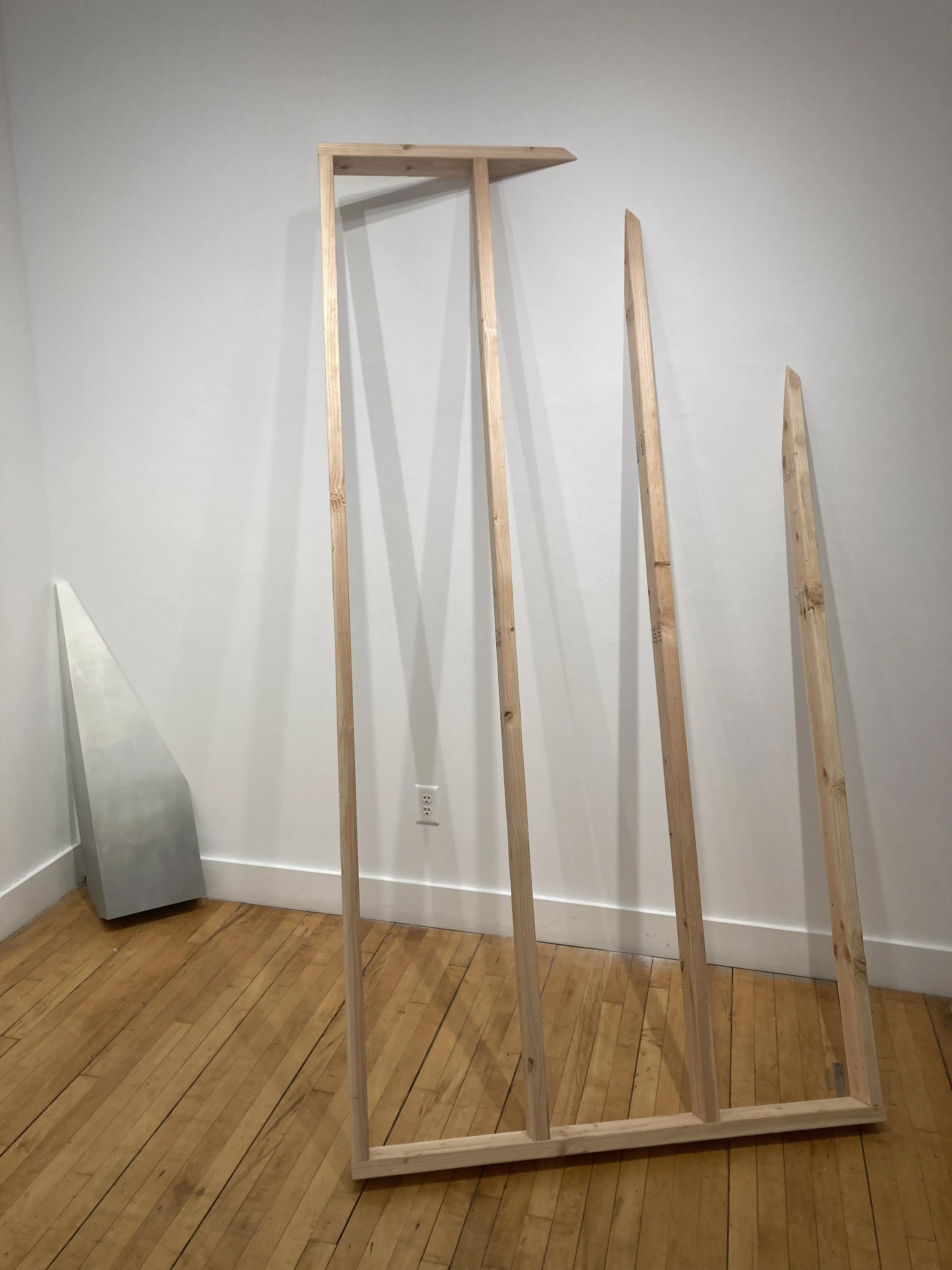 Minimalist wooden art installation with geometric shapes on a wooden floor in a gallery setting.