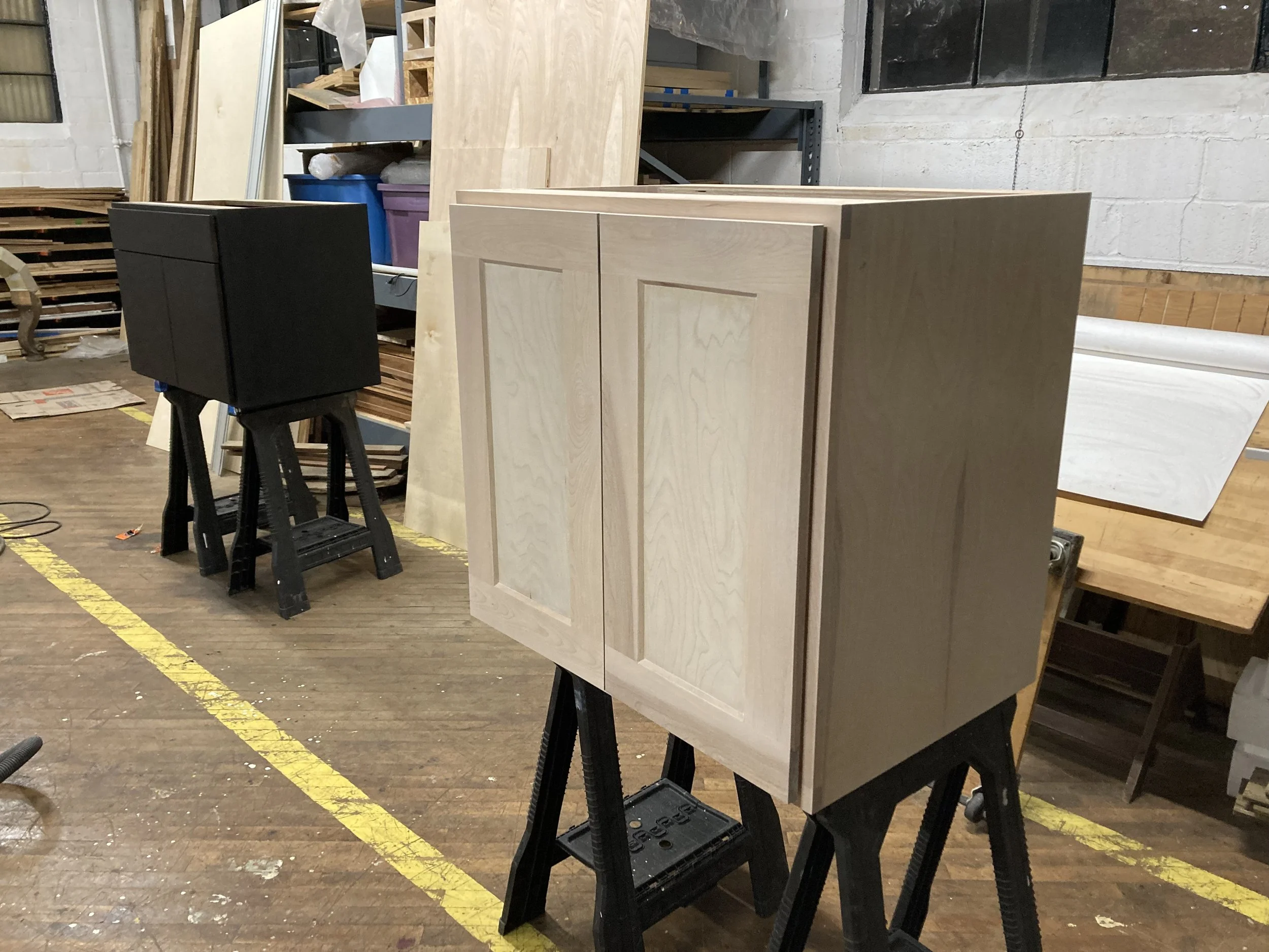Two unfinished wooden cabinets on sawhorses in a workshop.