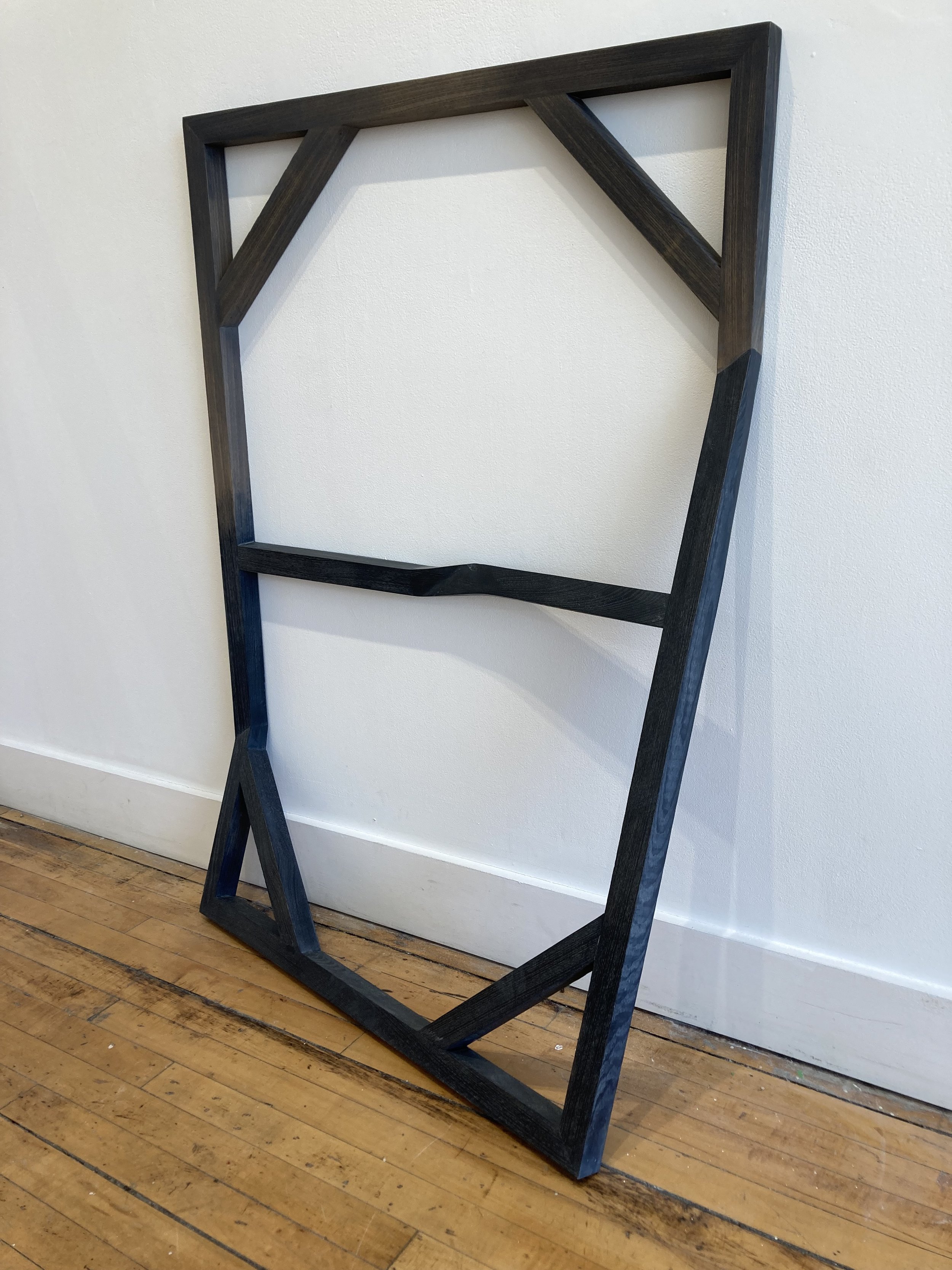 Wooden geometric structure leaning against a white wall on a wooden floor