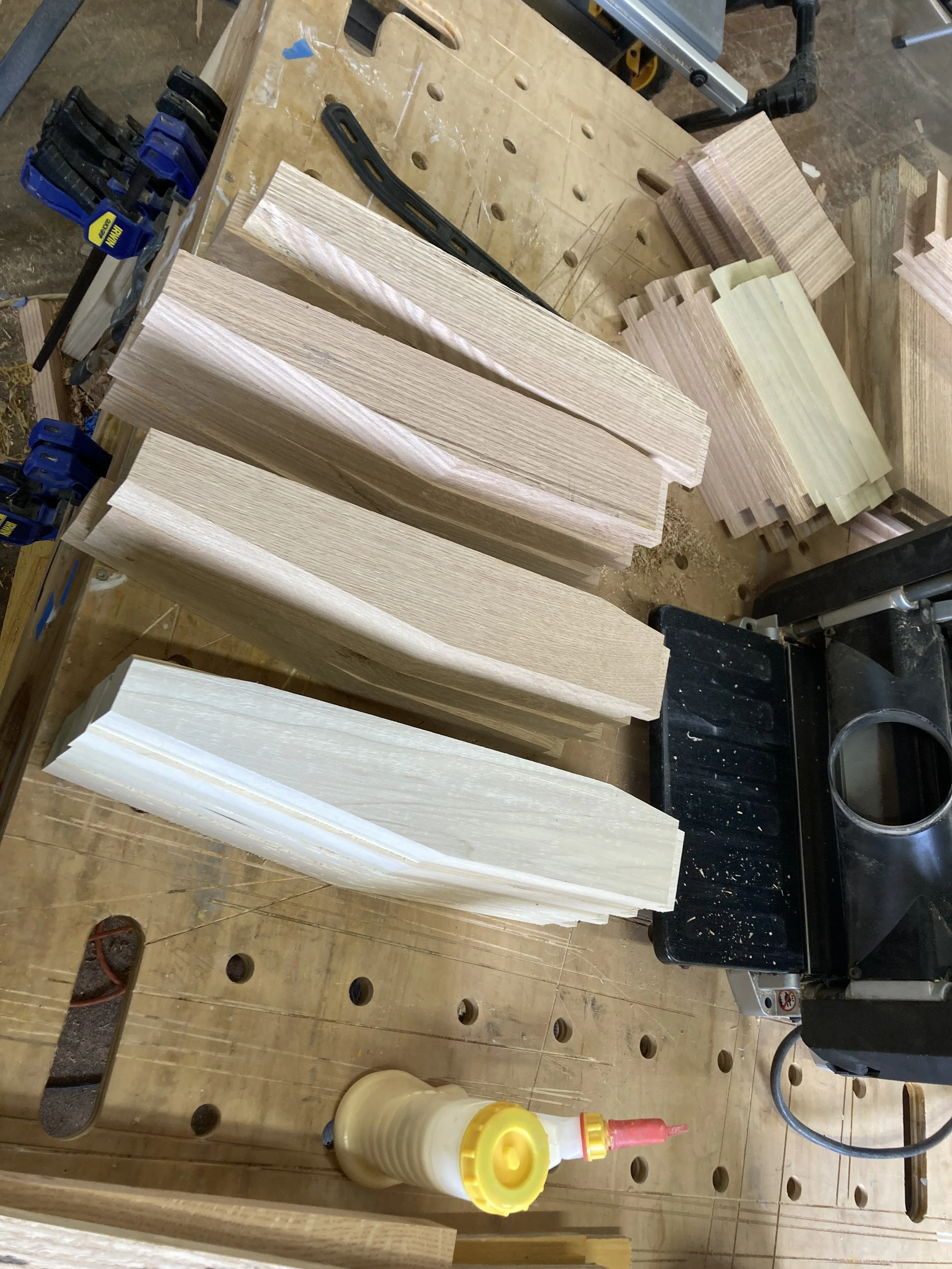 Pieces of cut wood on a workbench with clamps and a bottle of wood glue.