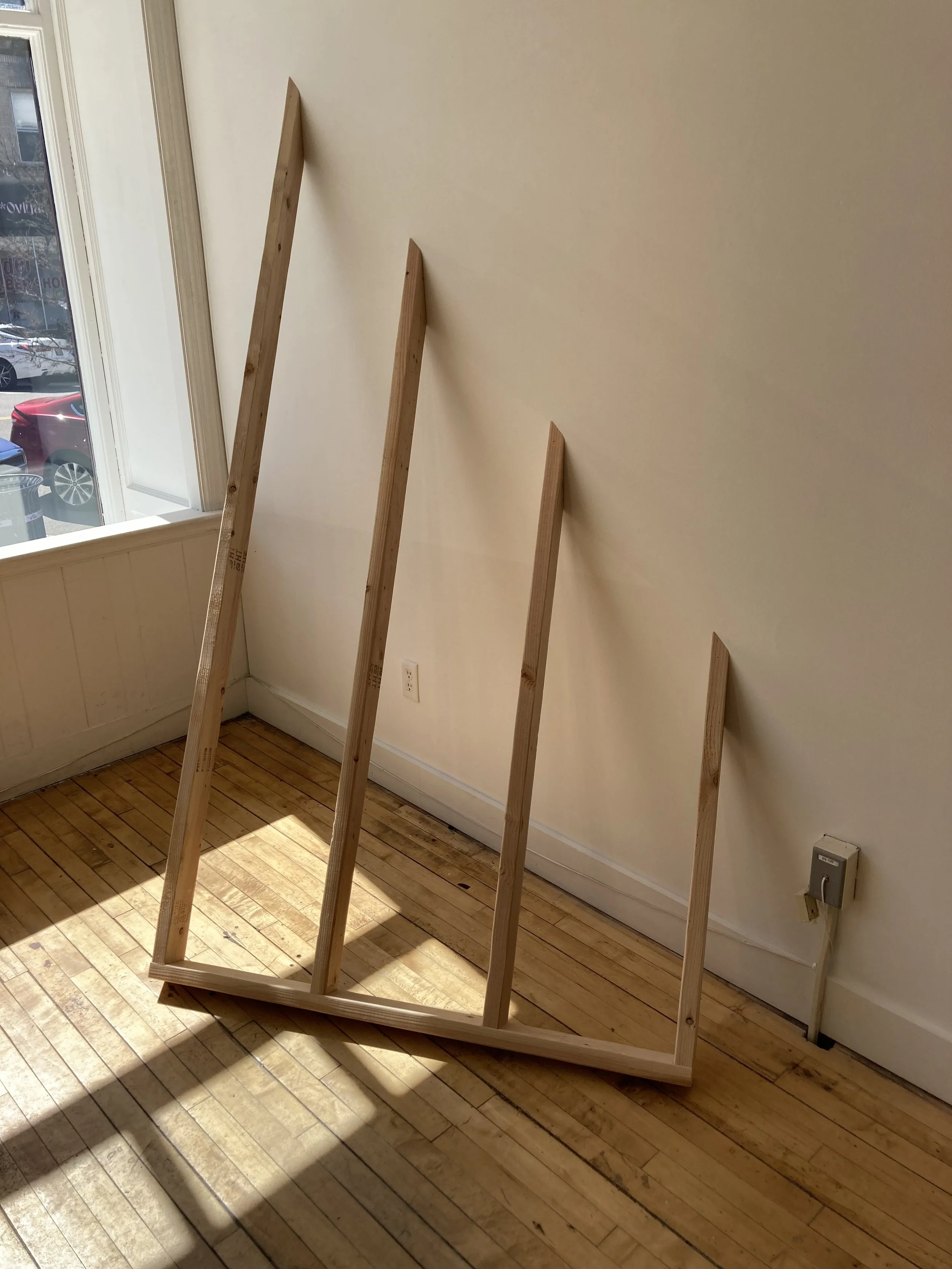Wooden frame with four beams leaning against a wall in a sunlit room with wooden floors.
