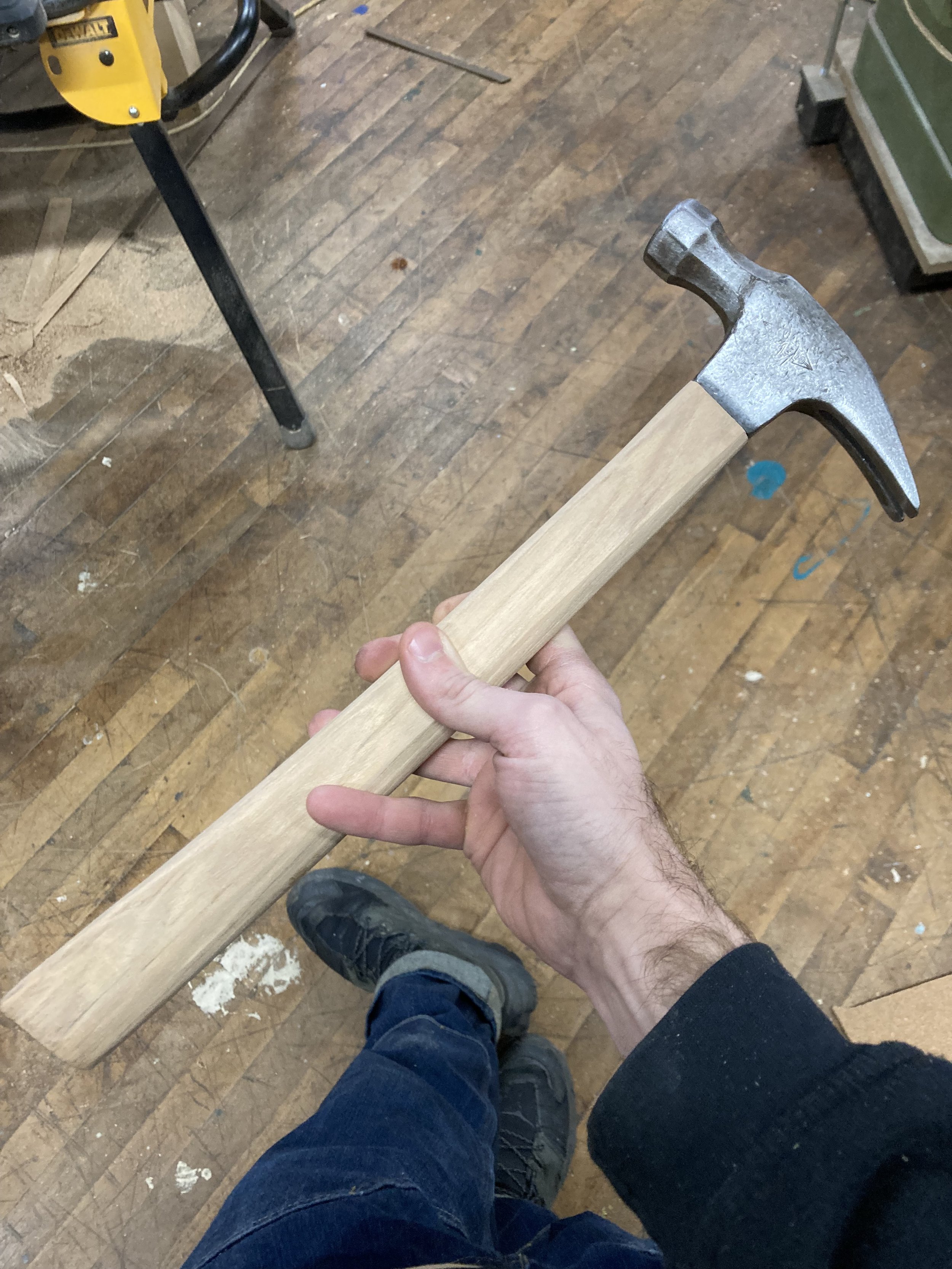 Person holding a claw hammer with a wooden handle, standing on a wooden floor.