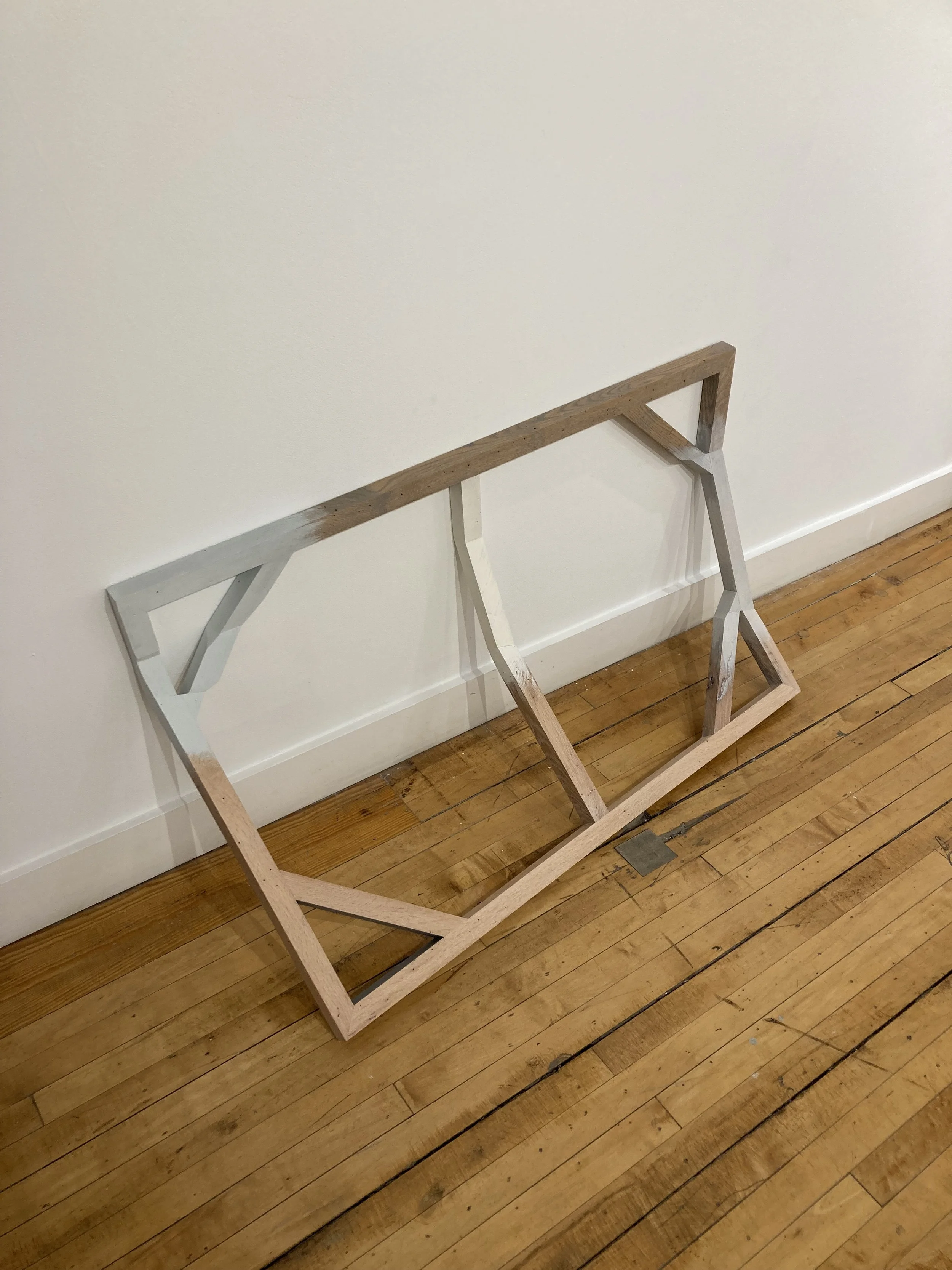 Wooden frame with angled supports leaning against a white wall on a wooden floor.