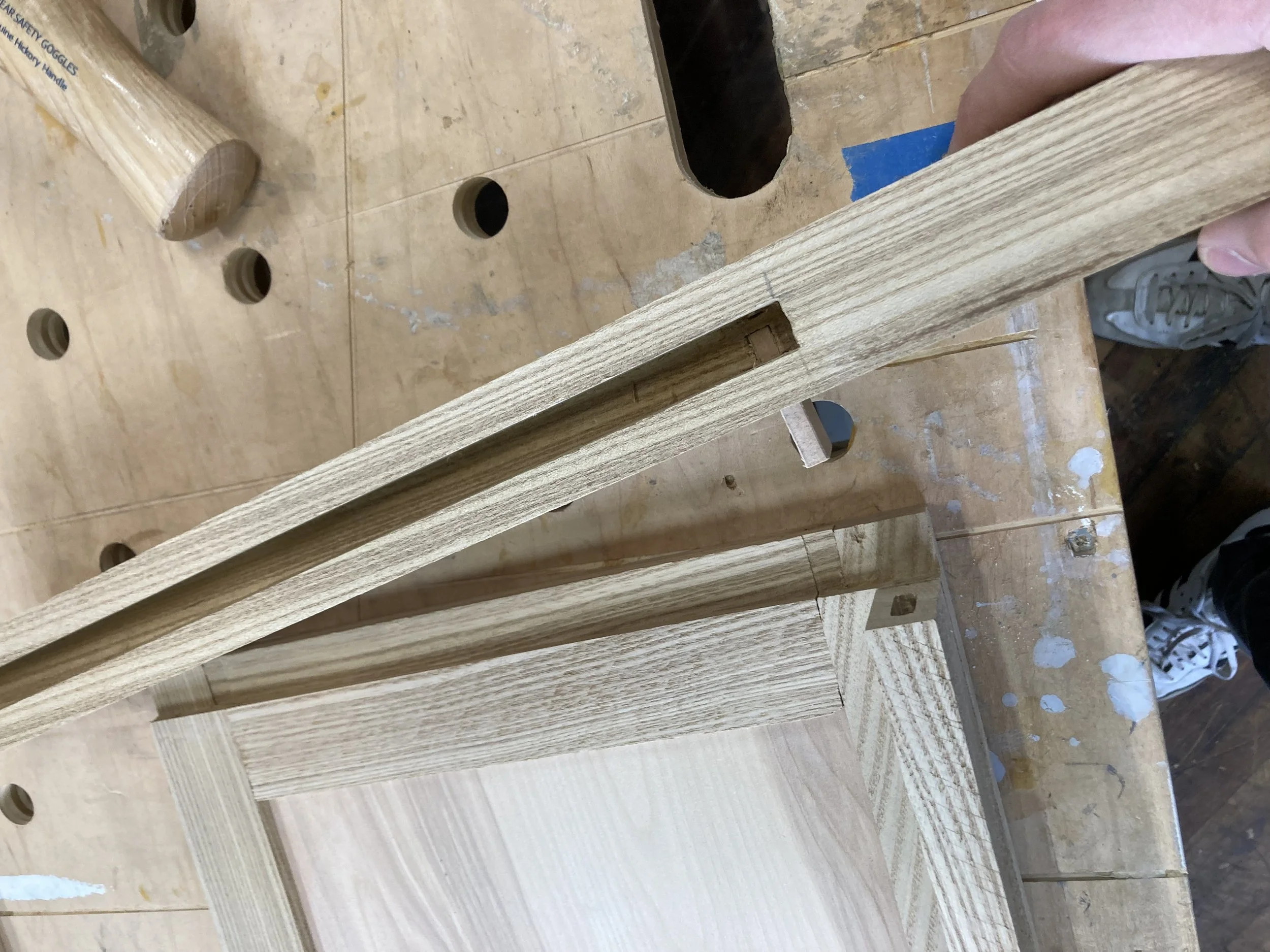 Woodworking joint detail on a wooden table with a wooden mallet and sneakers visible.
