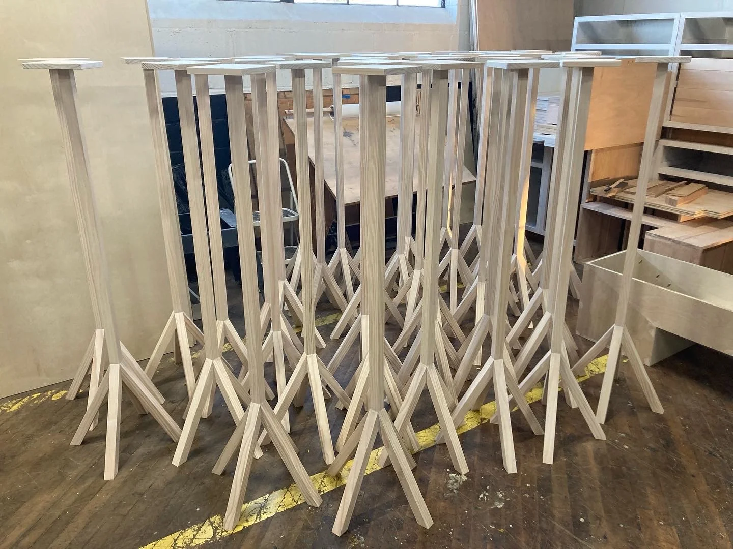 Several wooden stands with three-legged bases in a workshop setting.