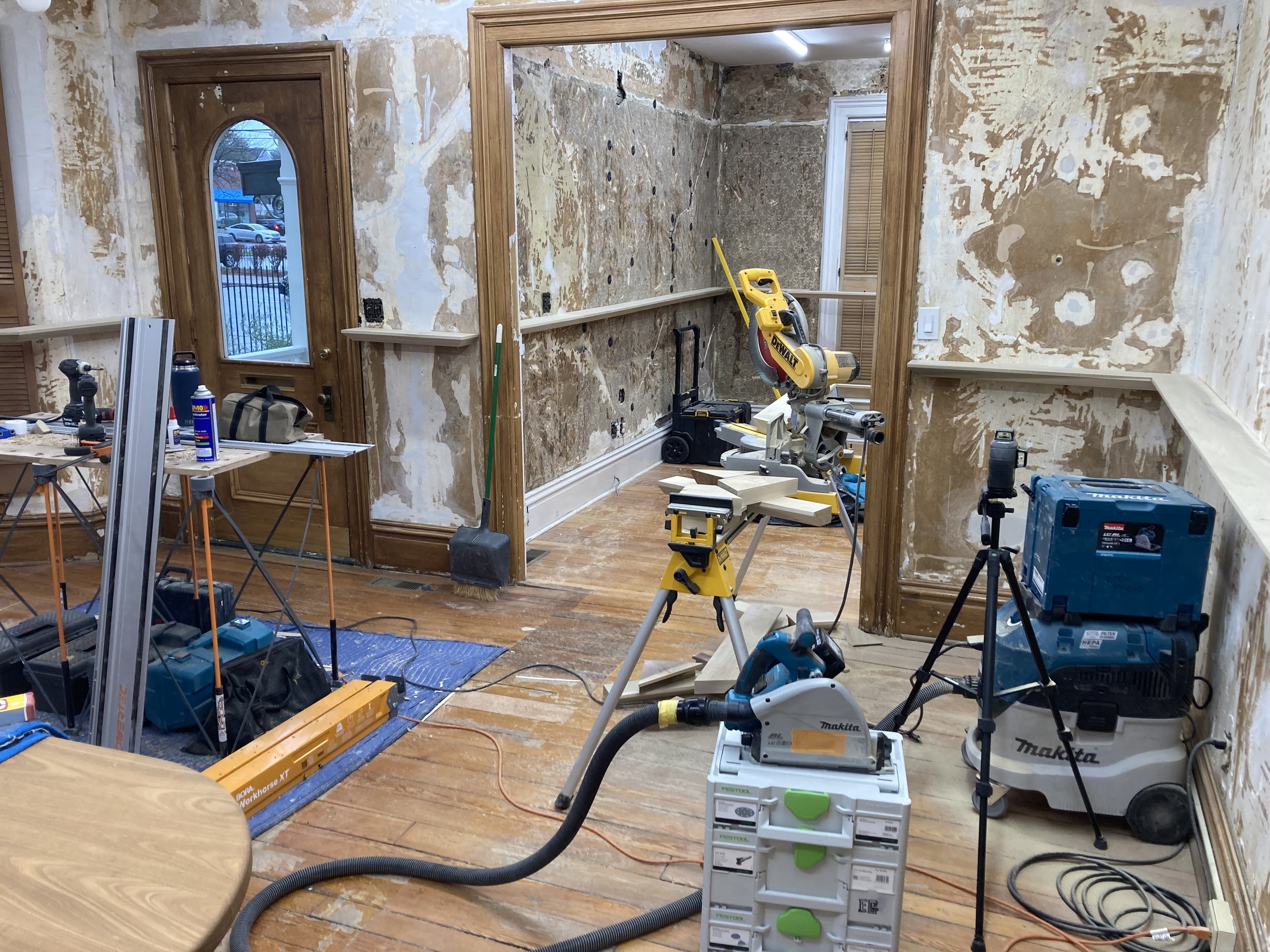 Room under renovation with construction tools, exposed walls, and wooden floor.