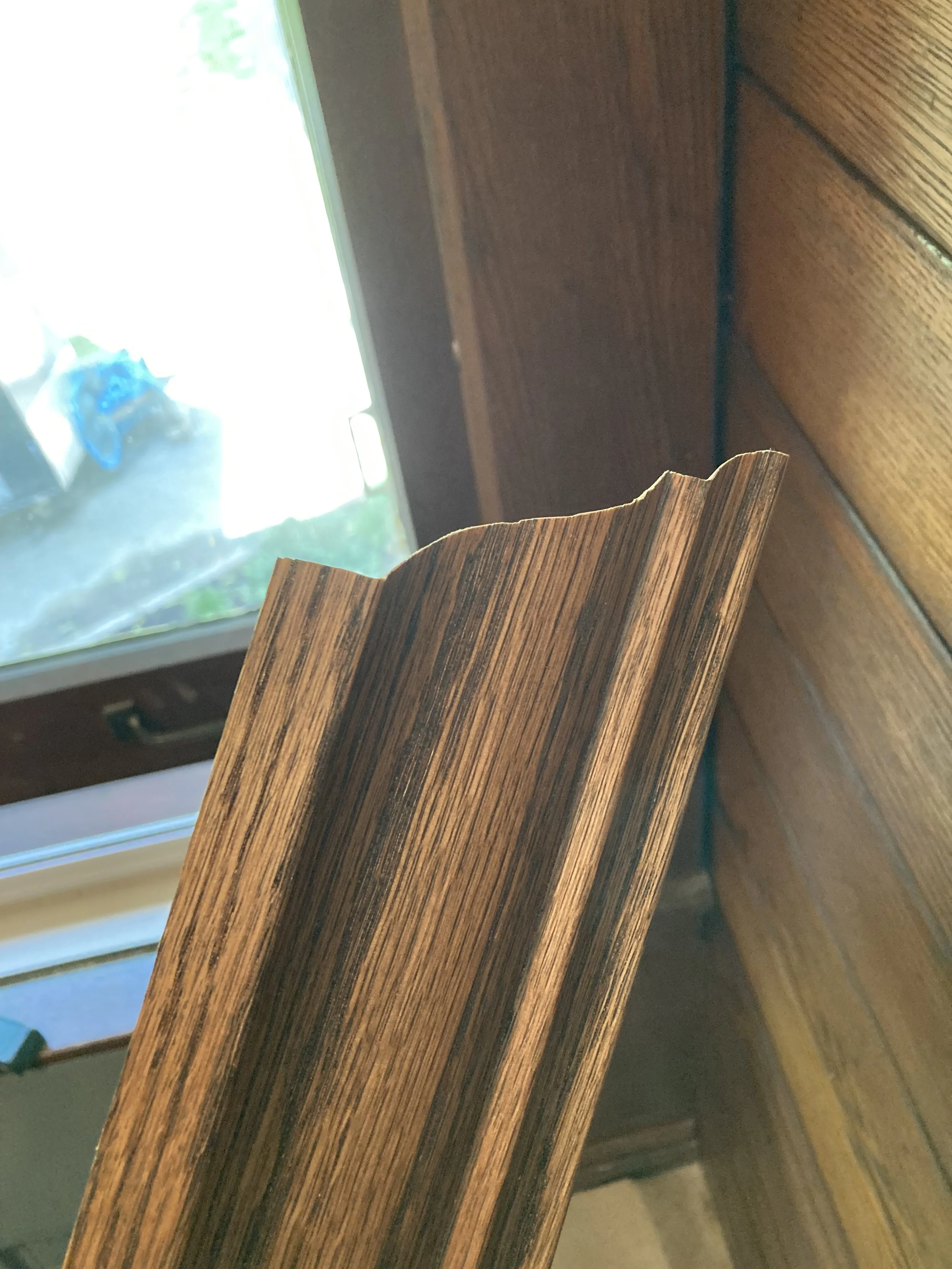 Brown wooden molding with a notched edge, positioned near a window with natural light.