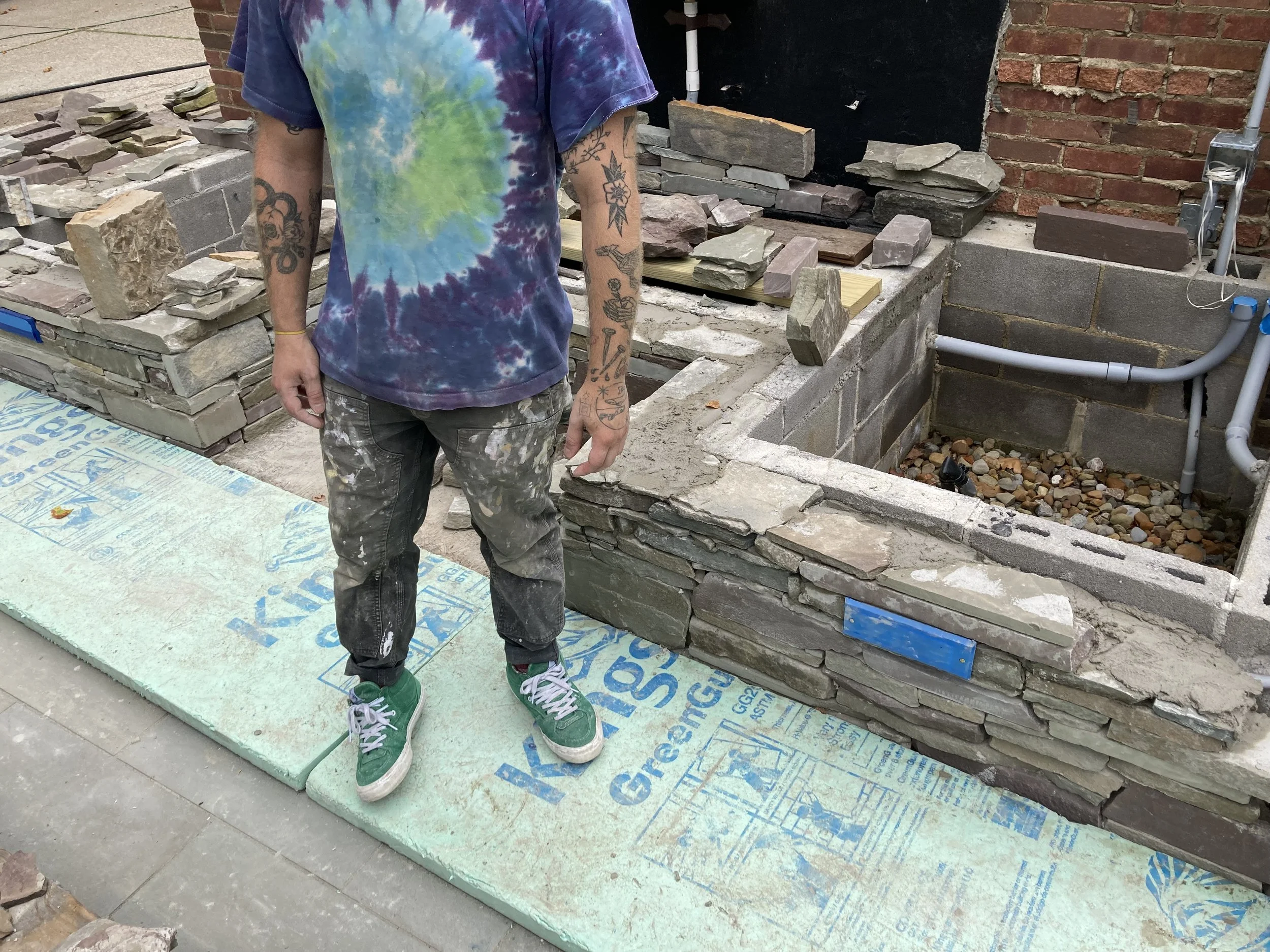 Person standing on insulation boards near stone wall construction site.