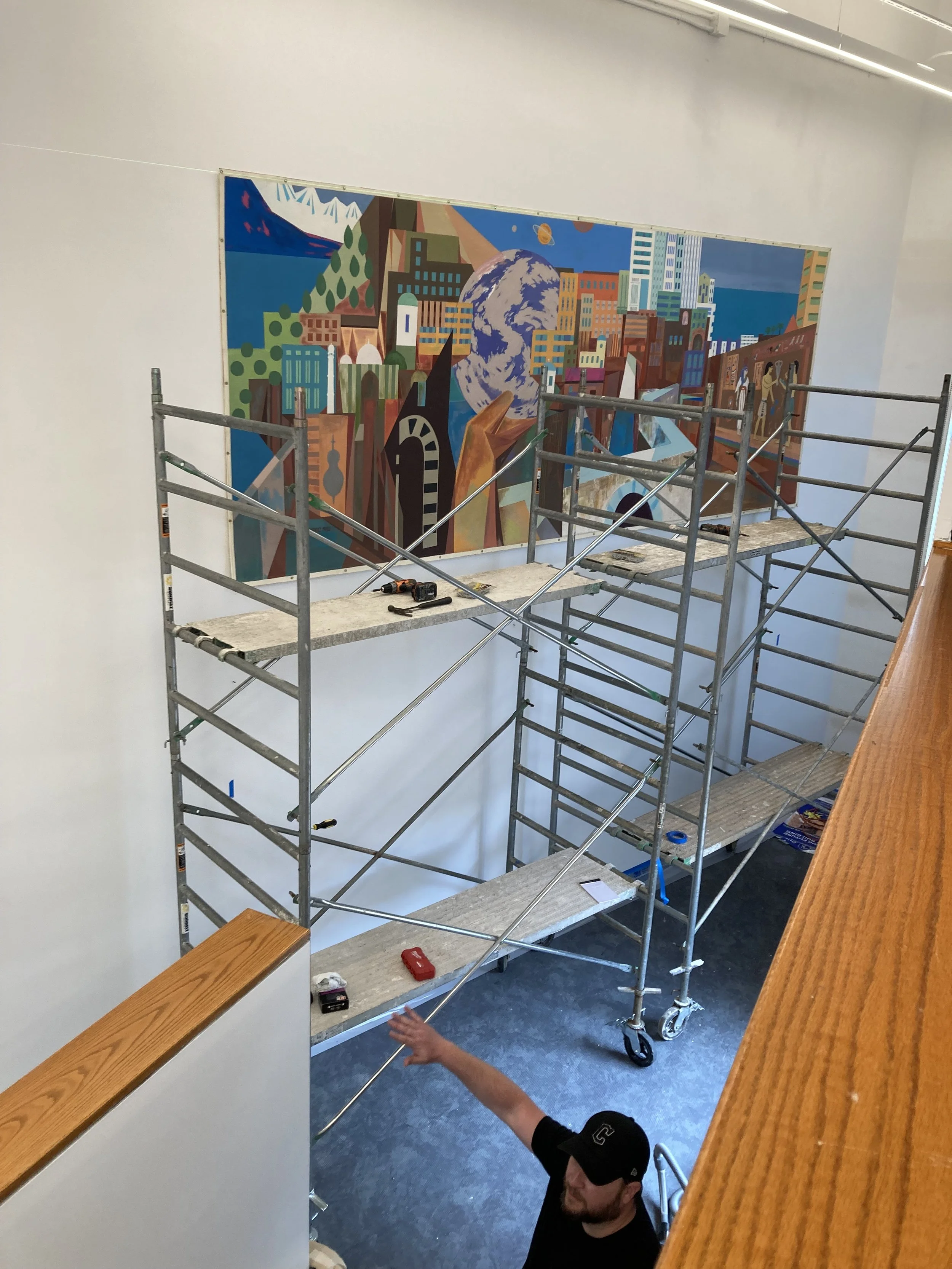 Person working on scaffolding near a colorful mural on a white wall.