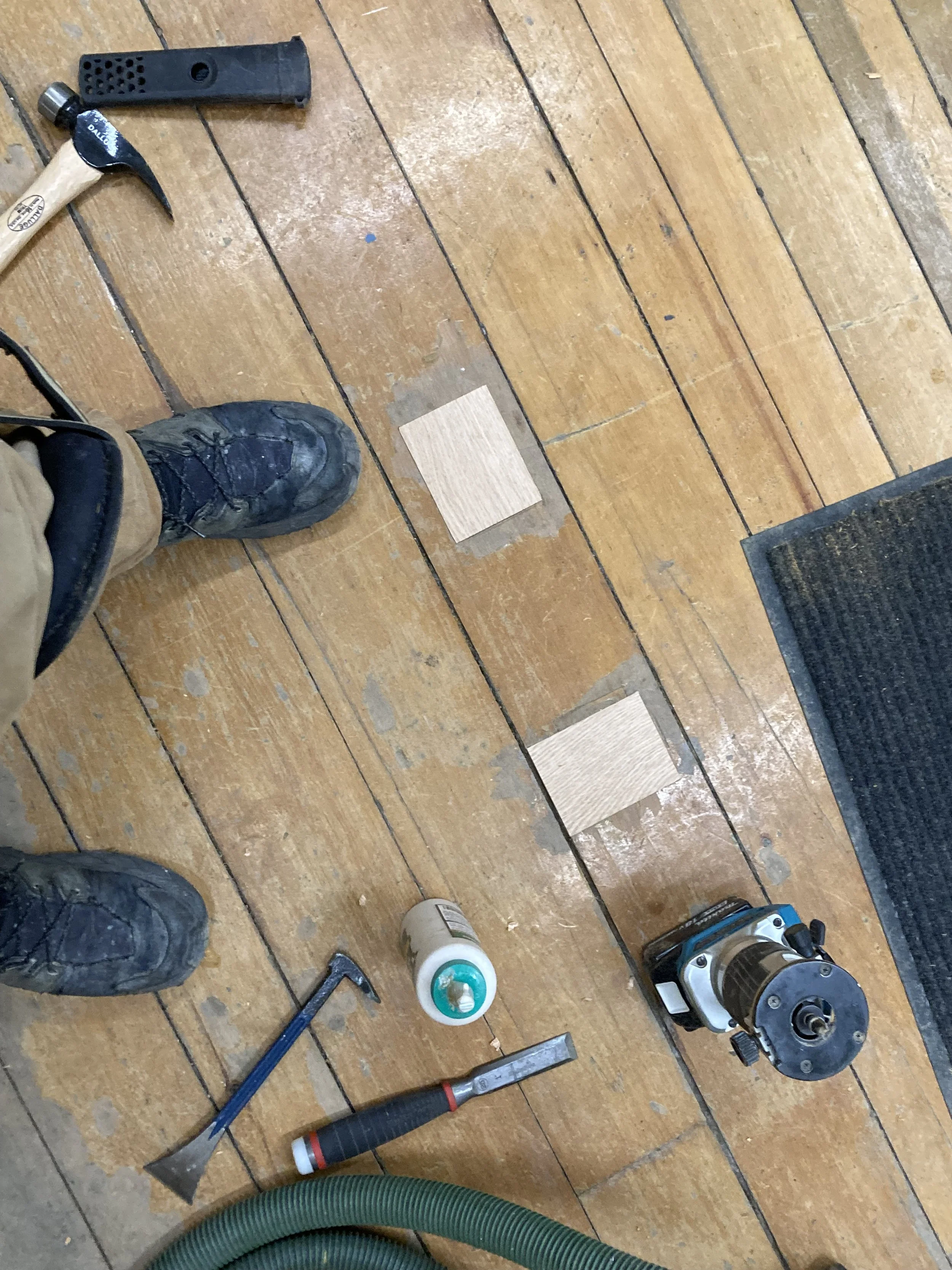 Wooden floor being repaired with tools and materials including a hammer, crowbar, chisel, wood glue, and a router.