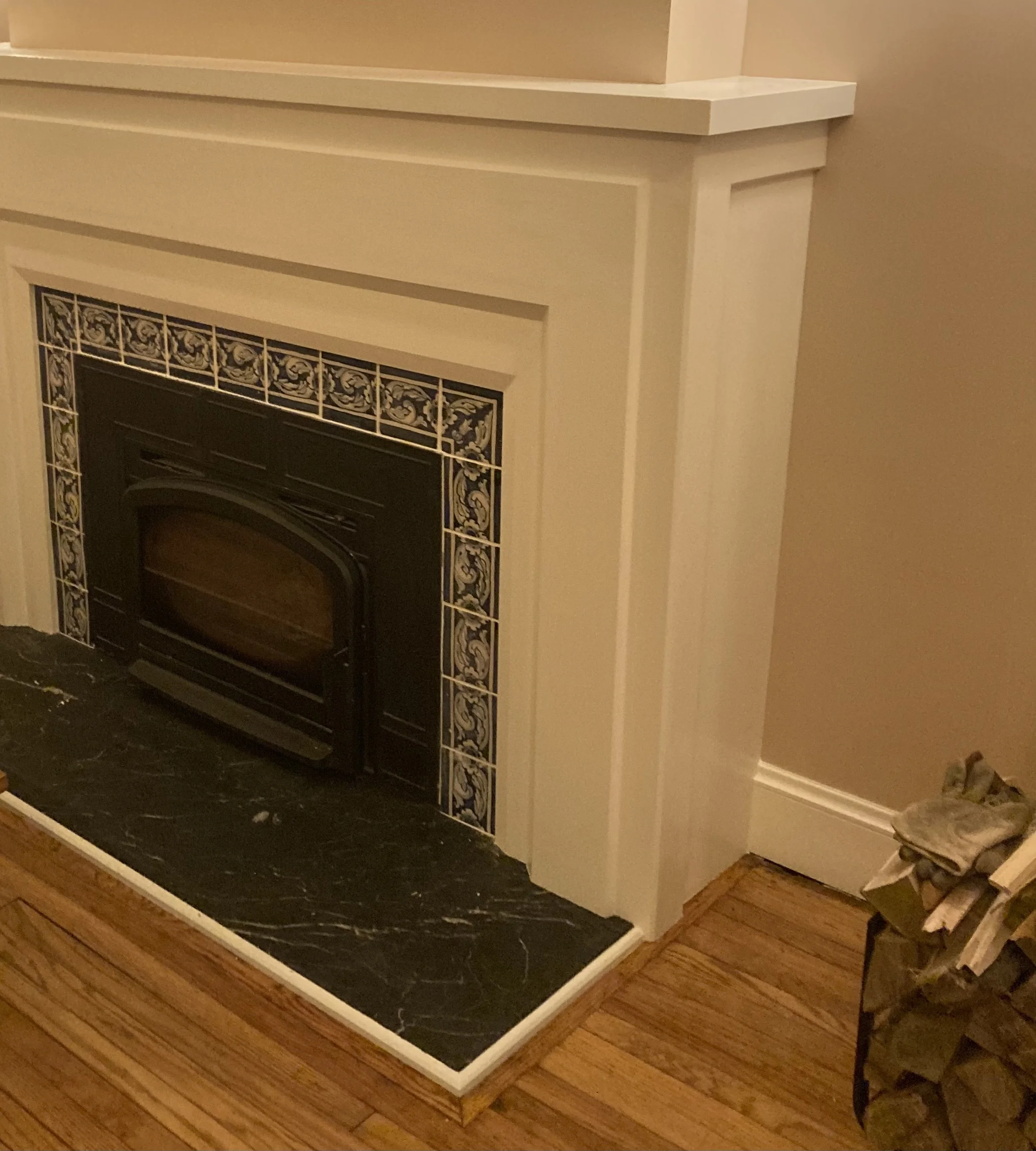 A modern fireplace with ornate black and white tile design and a black hearth, adjacent to a pile of firewood on a wooden floor.