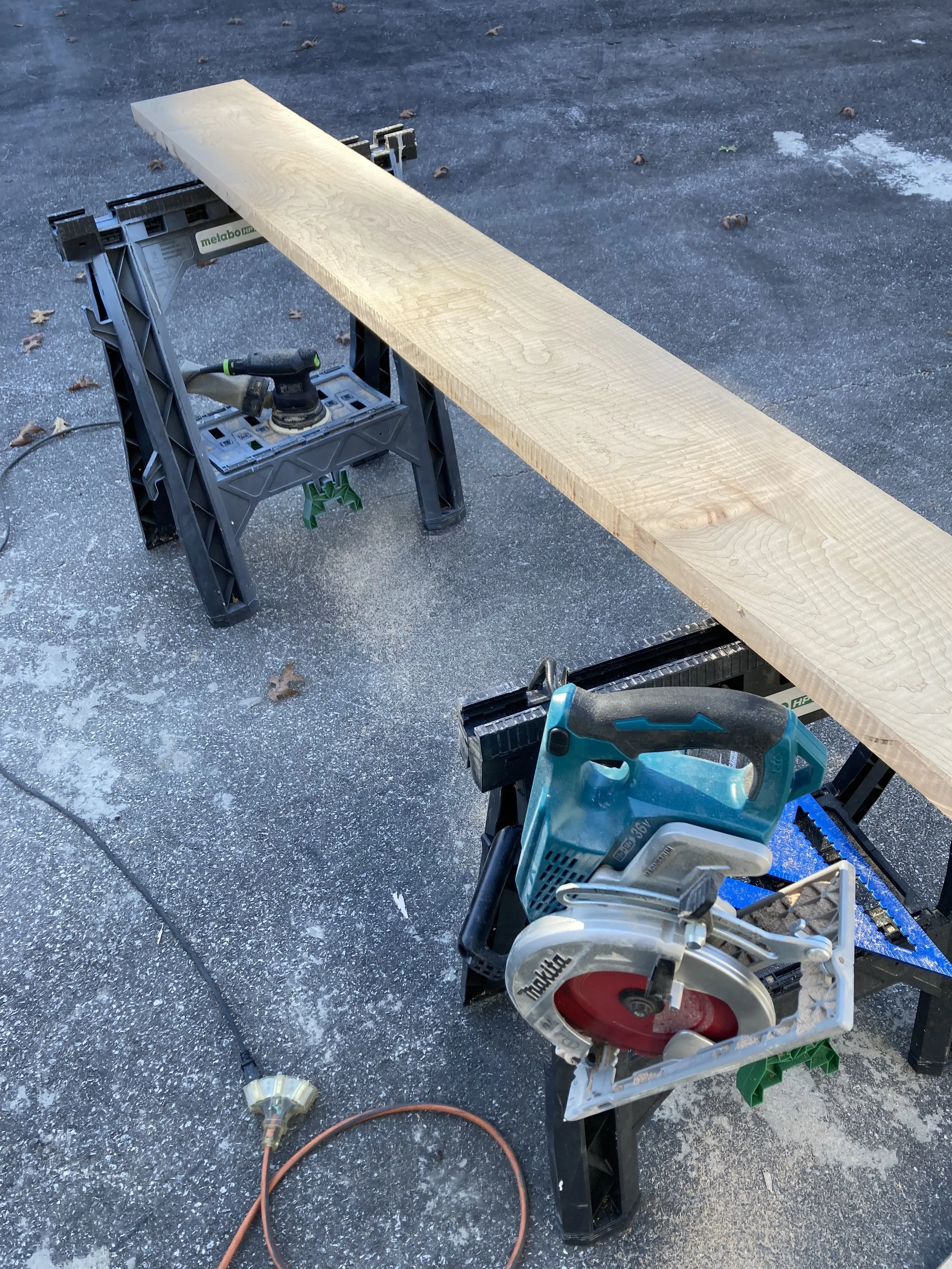Wood plank on sawhorses with circular saw and sander nearby.