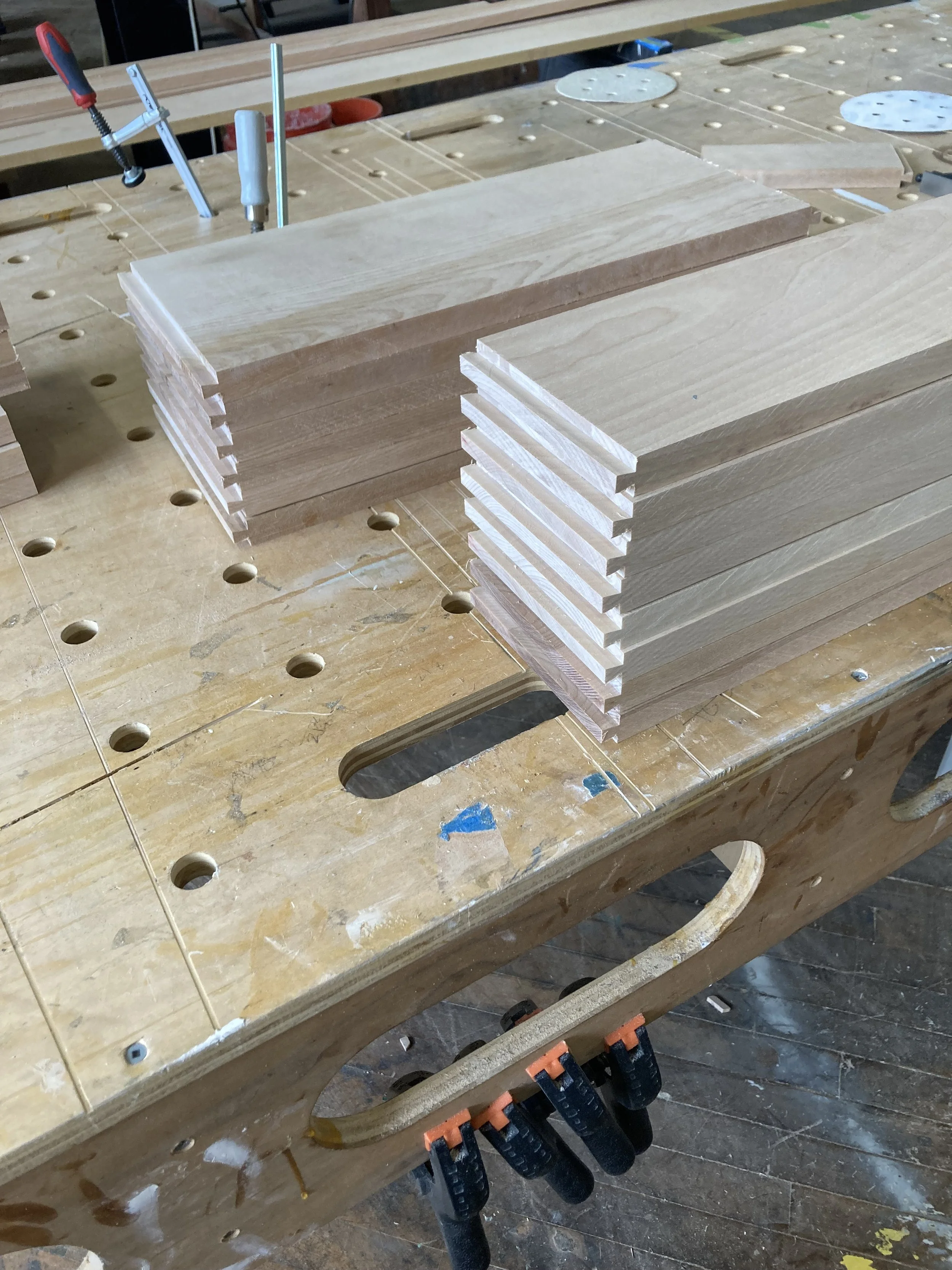 Stack of wooden boards with grooves on the edges, placed on a workbench with clamps and tools in a woodworking shop.