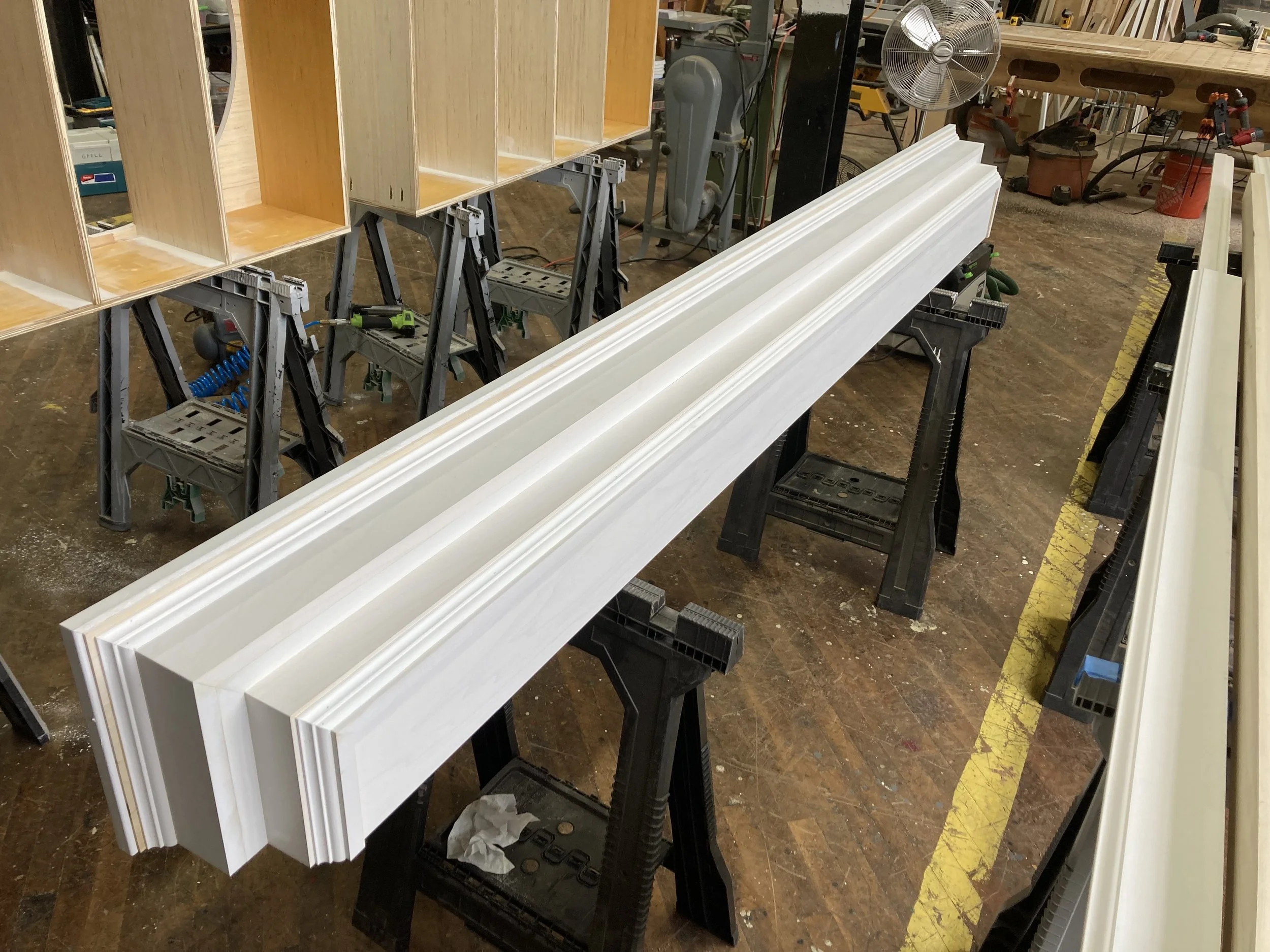 Wooden molding pieces supported by sawhorses in a workshop.
