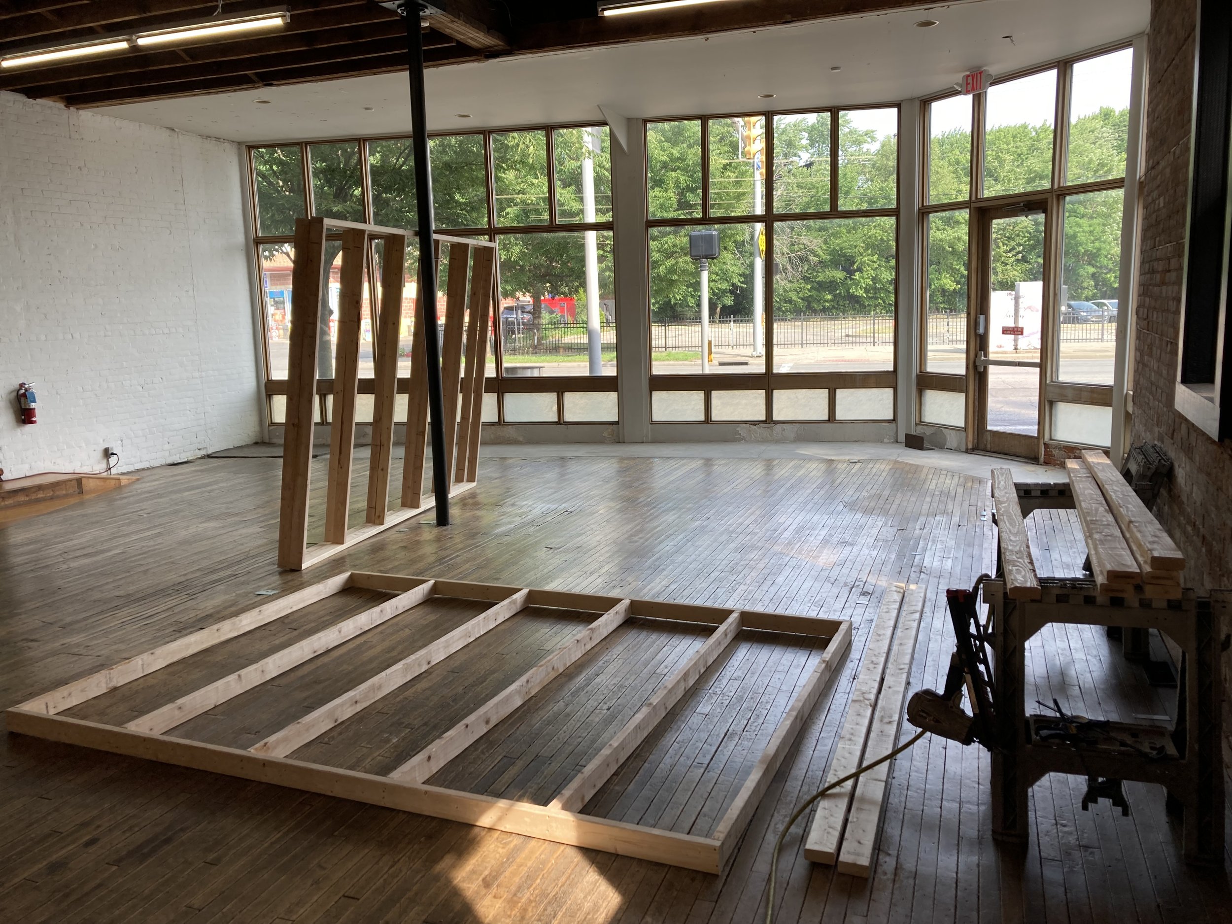 Interior of an unfinished room with wooden floor frames and large windows.