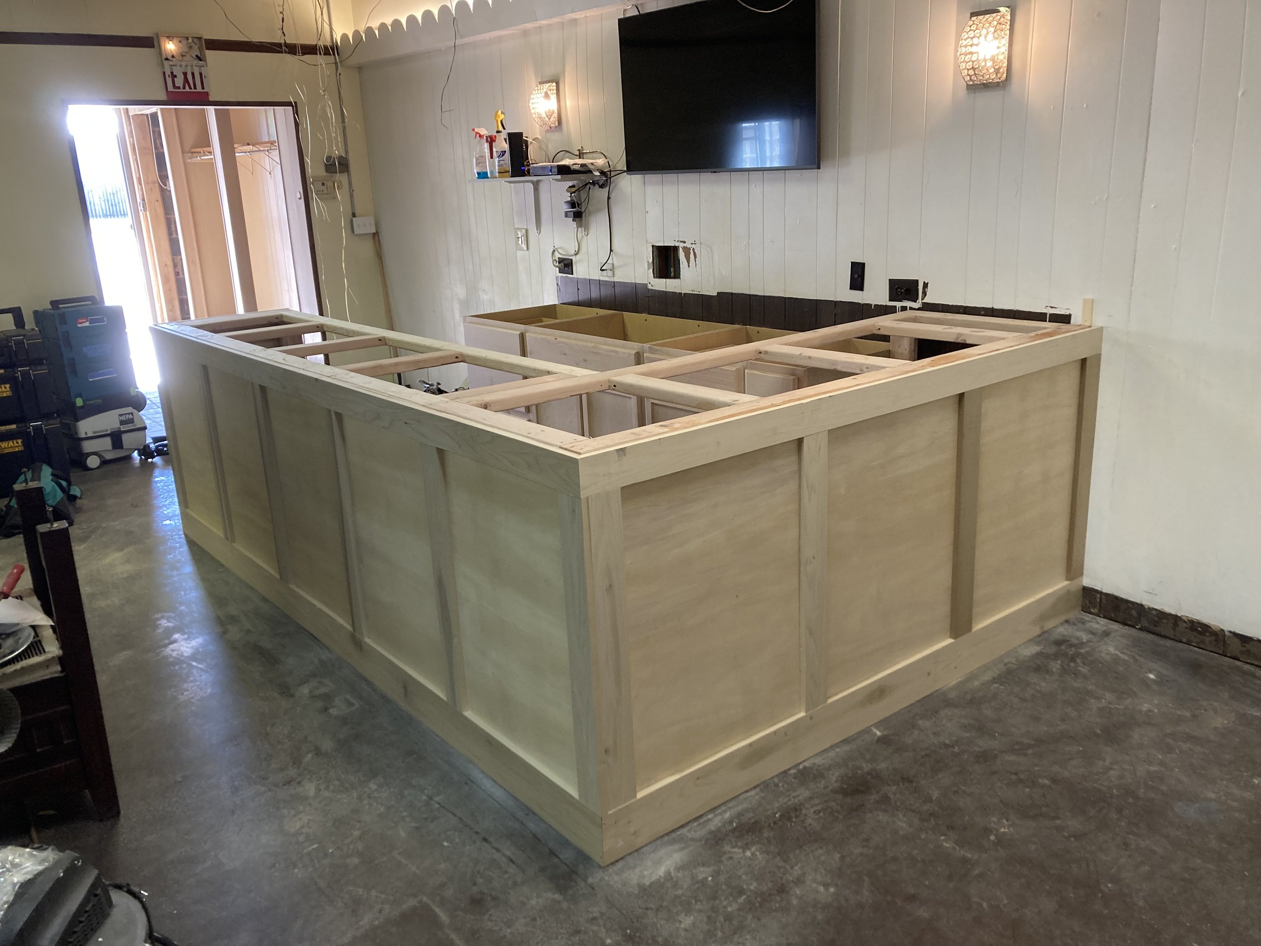 Partially constructed bar counter in room with wood paneling and exposed beams