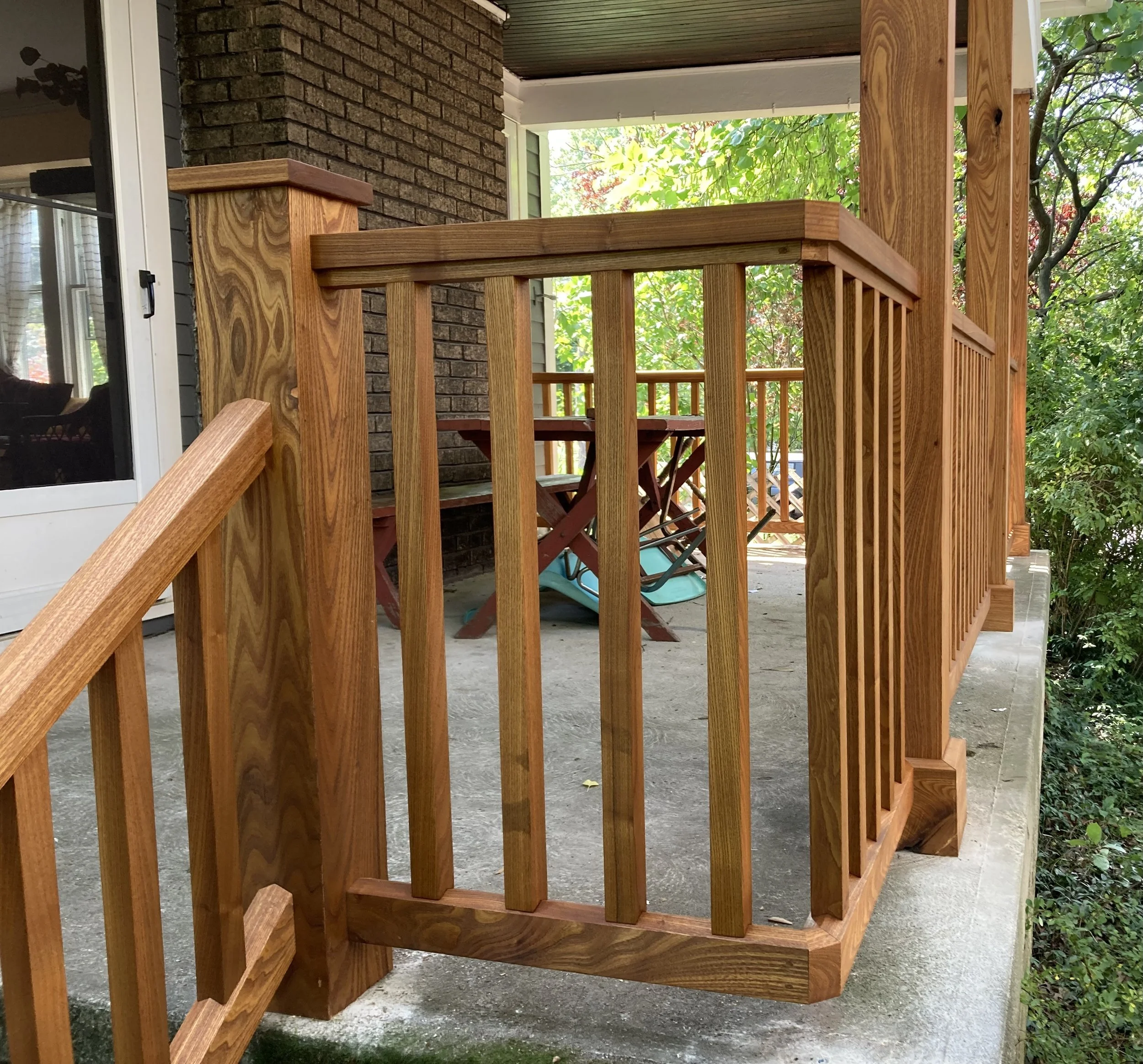 Wooden porch railing and furniture with a brick wall backdrop