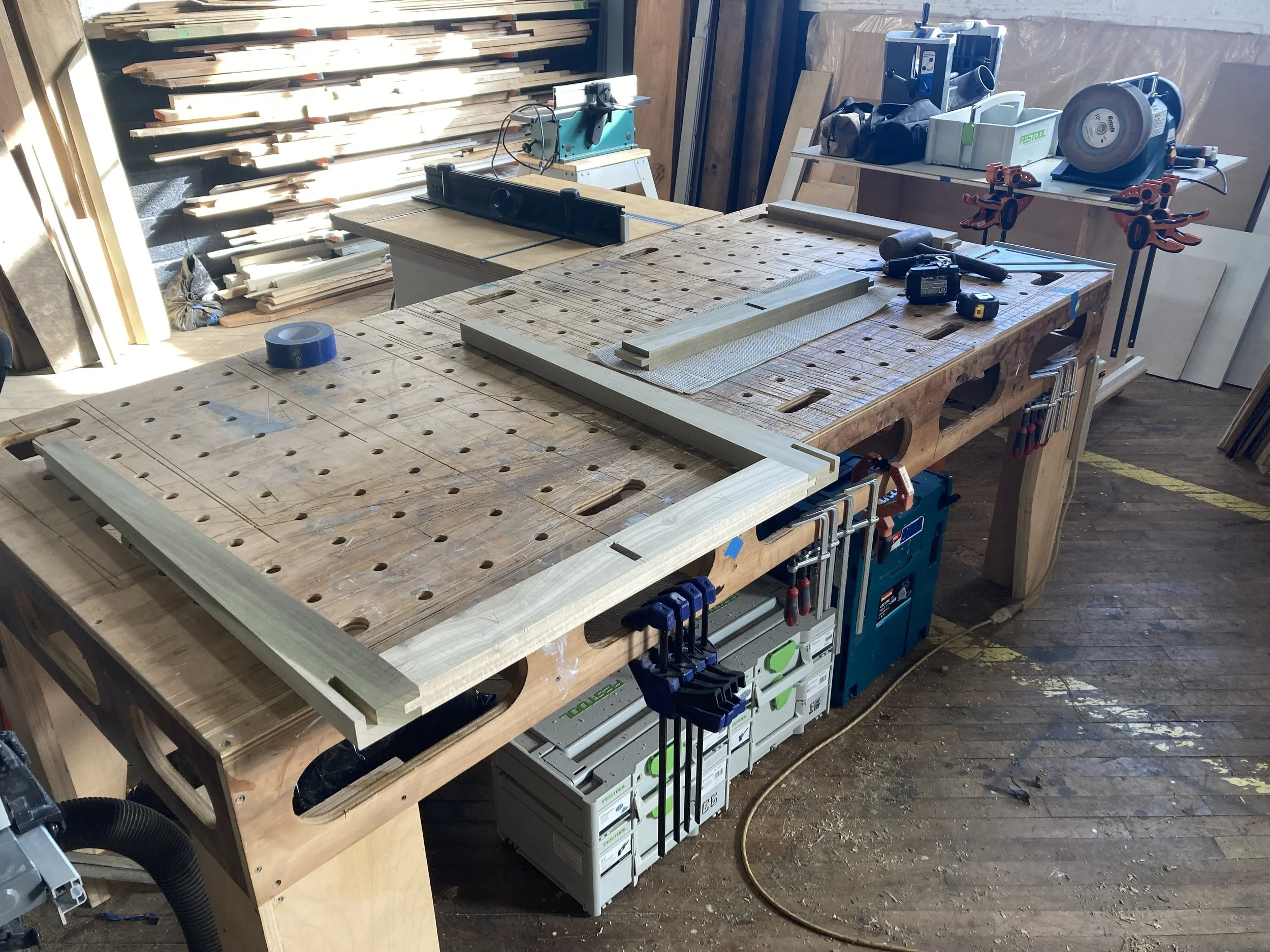 Woodworking table with tools, clamps, and wood pieces in a workshop setting.