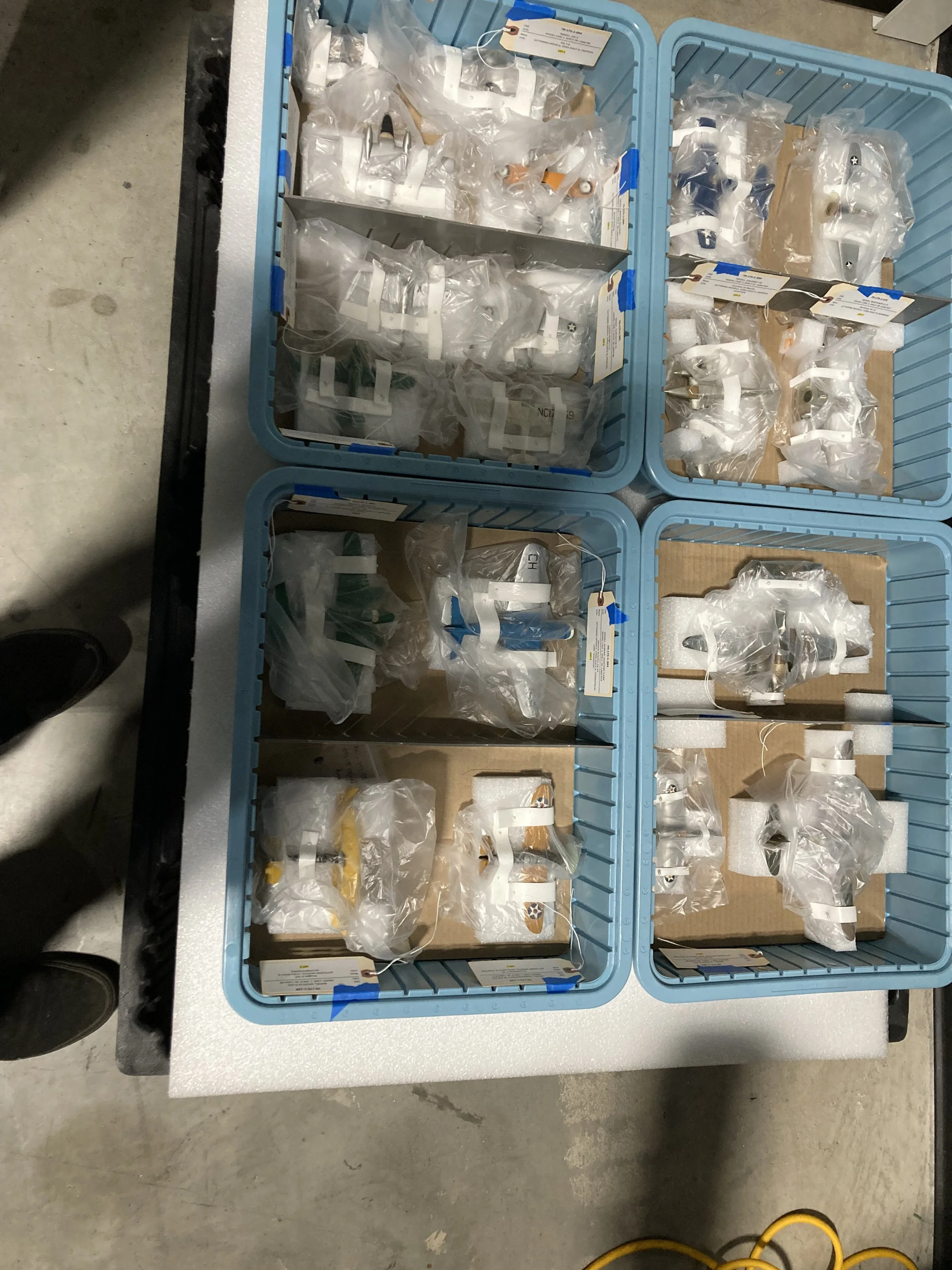 Plastic bins containing model airplanes, each individually wrapped in clear plastic and organized with labels.