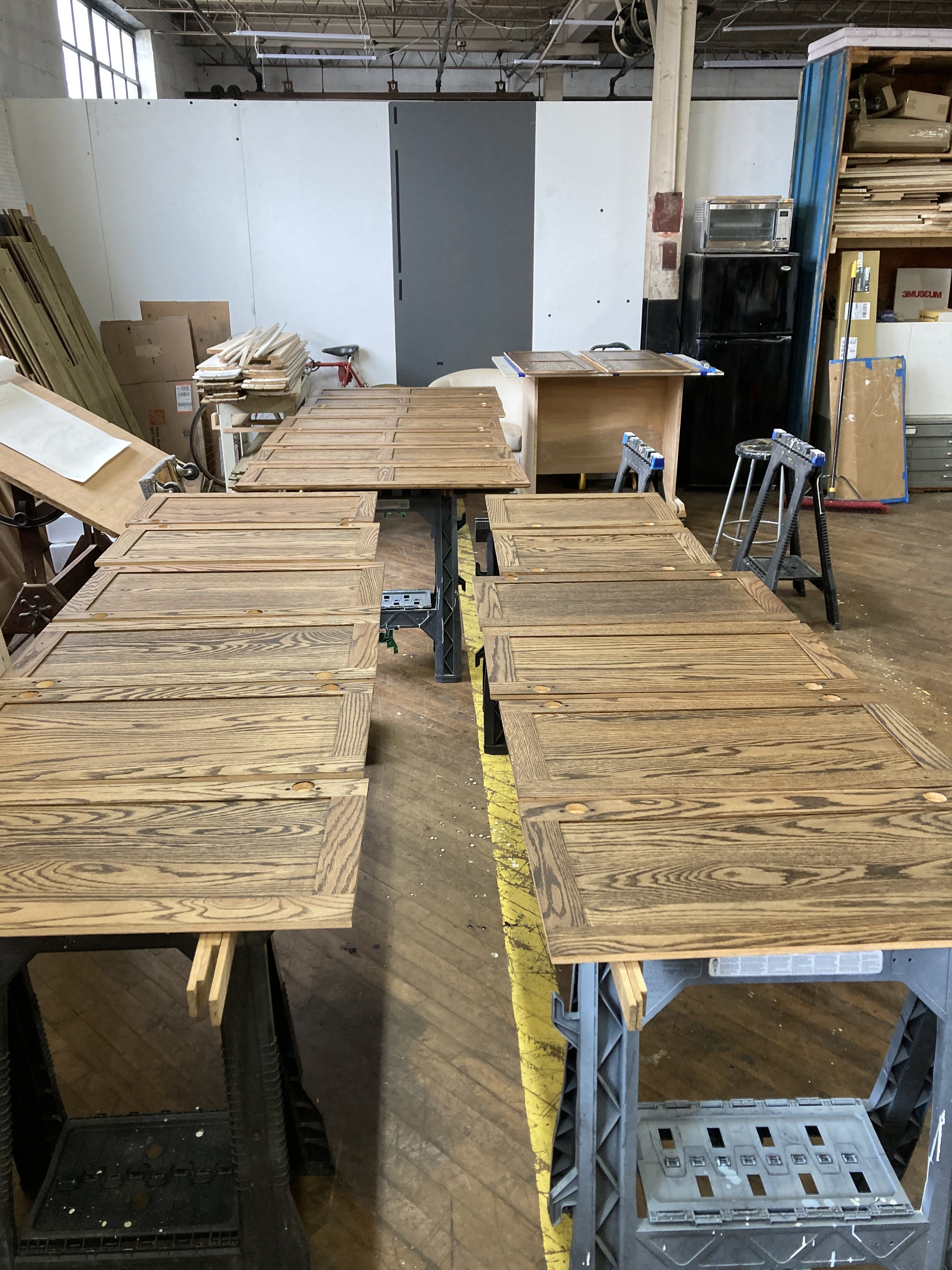 Wooden cabinet doors arranged on sawhorses in a workshop setting.