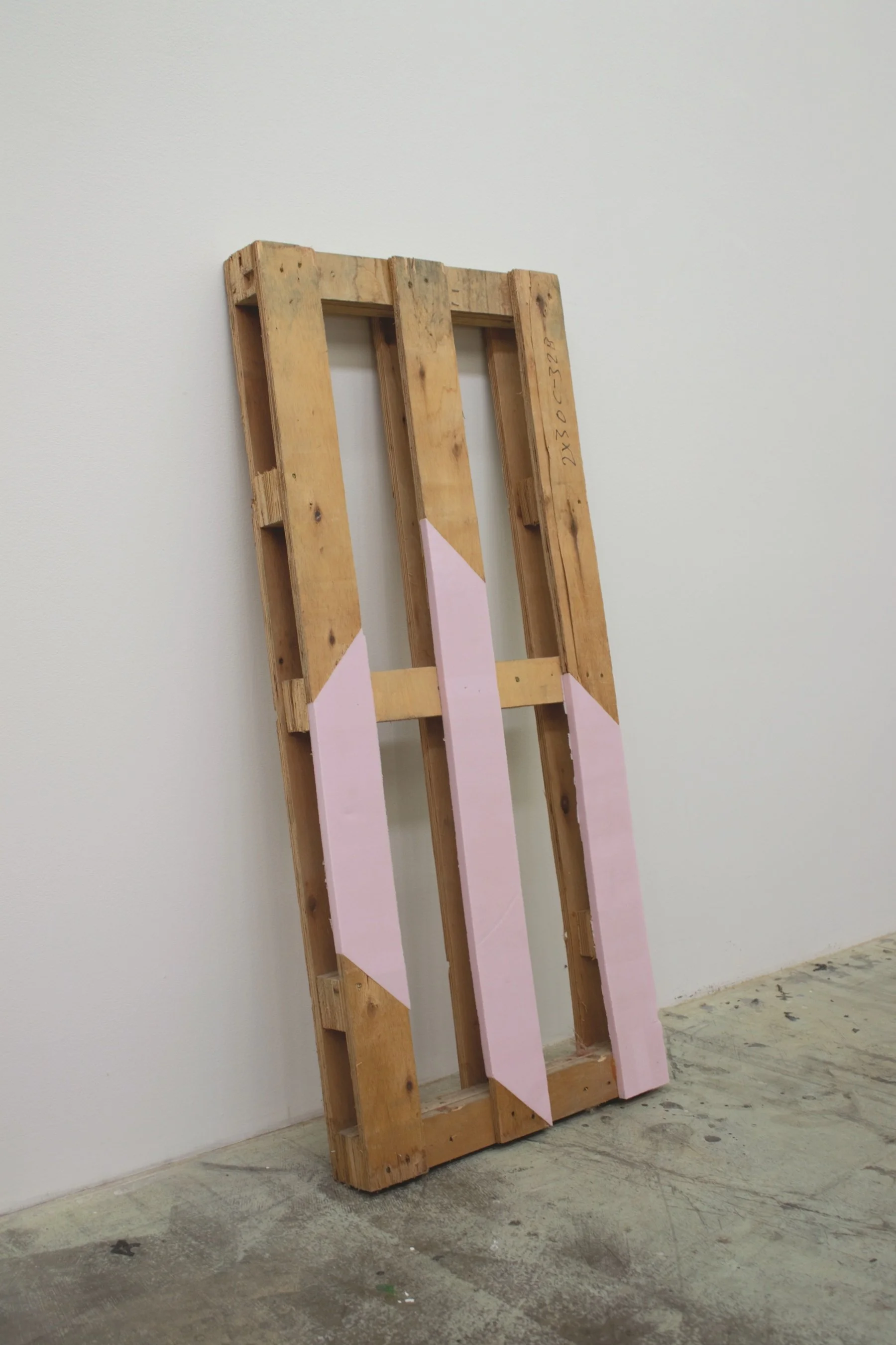 Wooden pallet leaning against wall with pink geometric shapes attached.