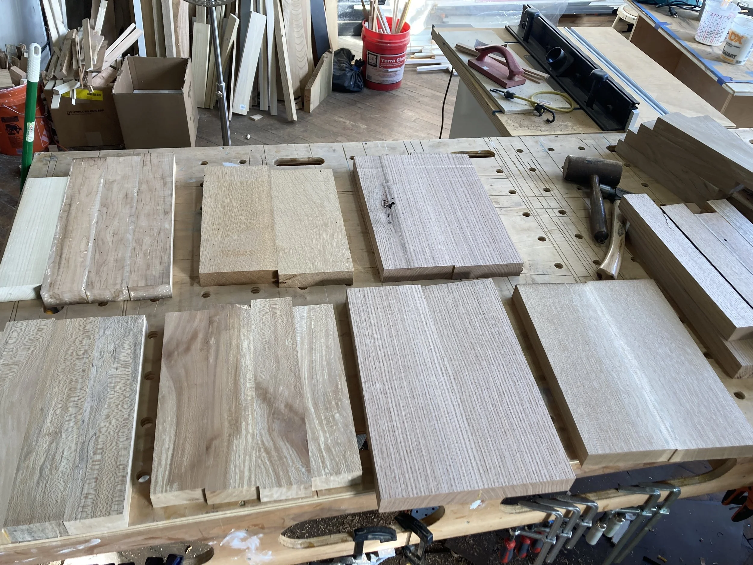 Wood workshop with various wooden planks on workbench, hand tools, and wood pieces in background.