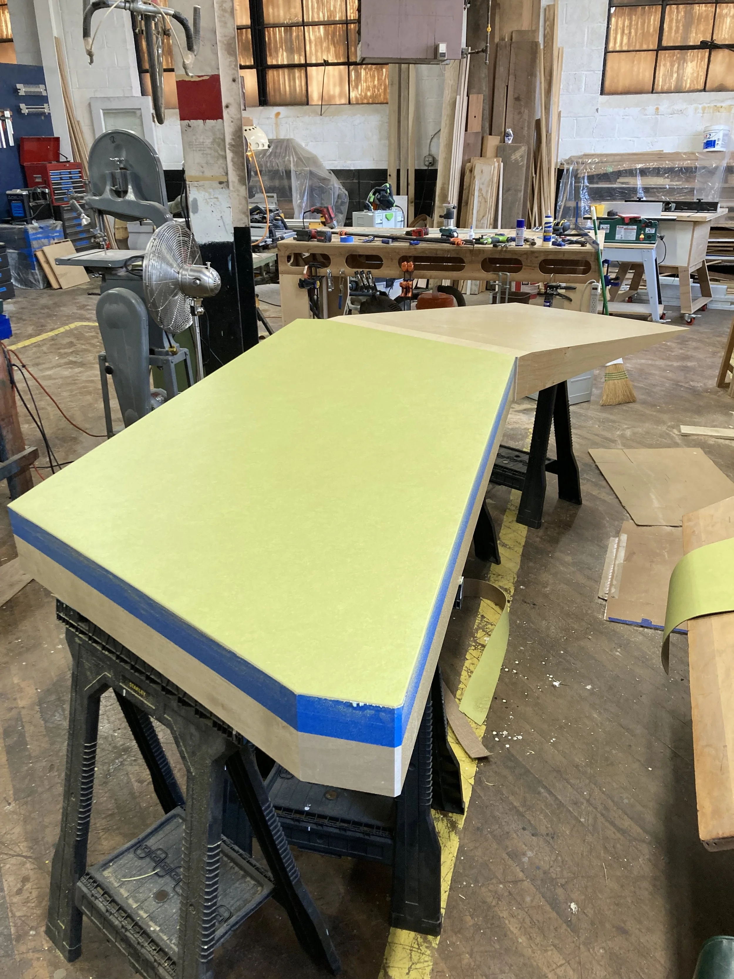 Woodworking shop with tools and workbenches, featuring a large piece of wood on sawhorses.