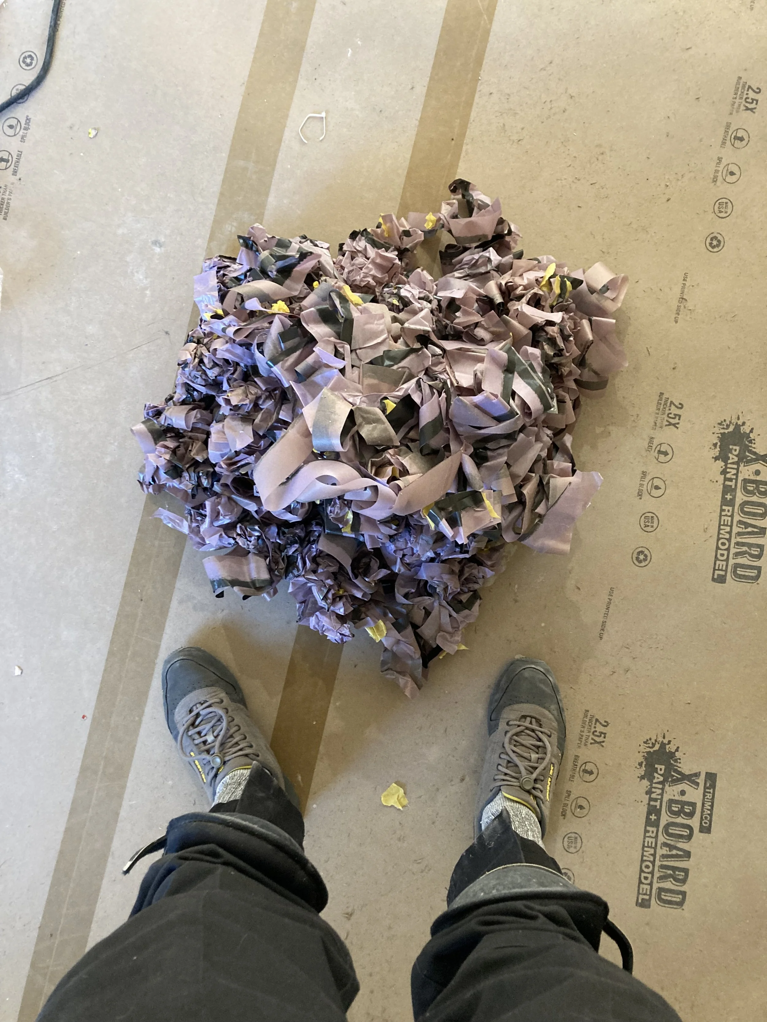Pile of crumpled painter's tape on protective floor covering, worker's feet in view