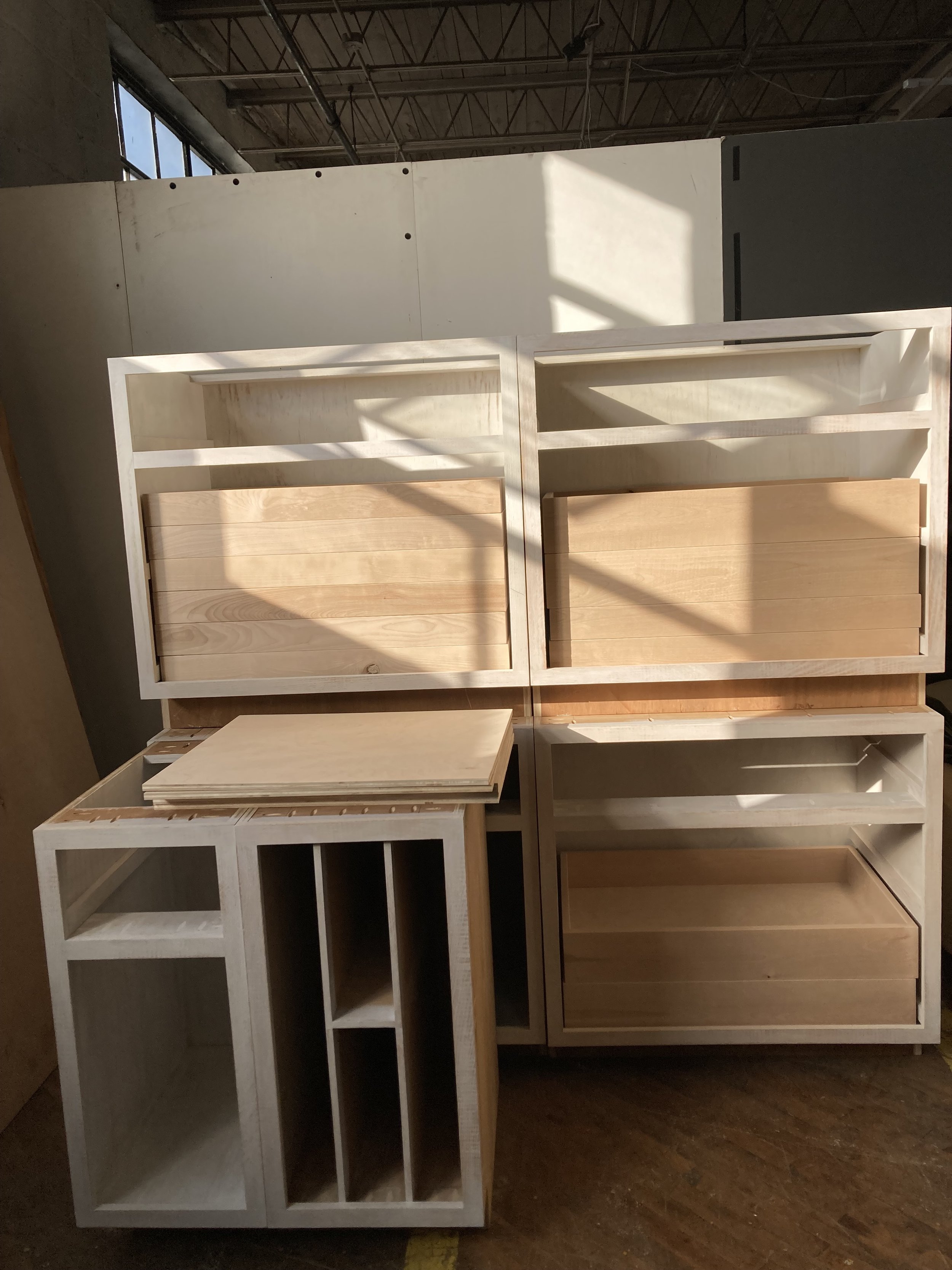Unfinished wooden cabinets and shelves in a workshop with natural light.