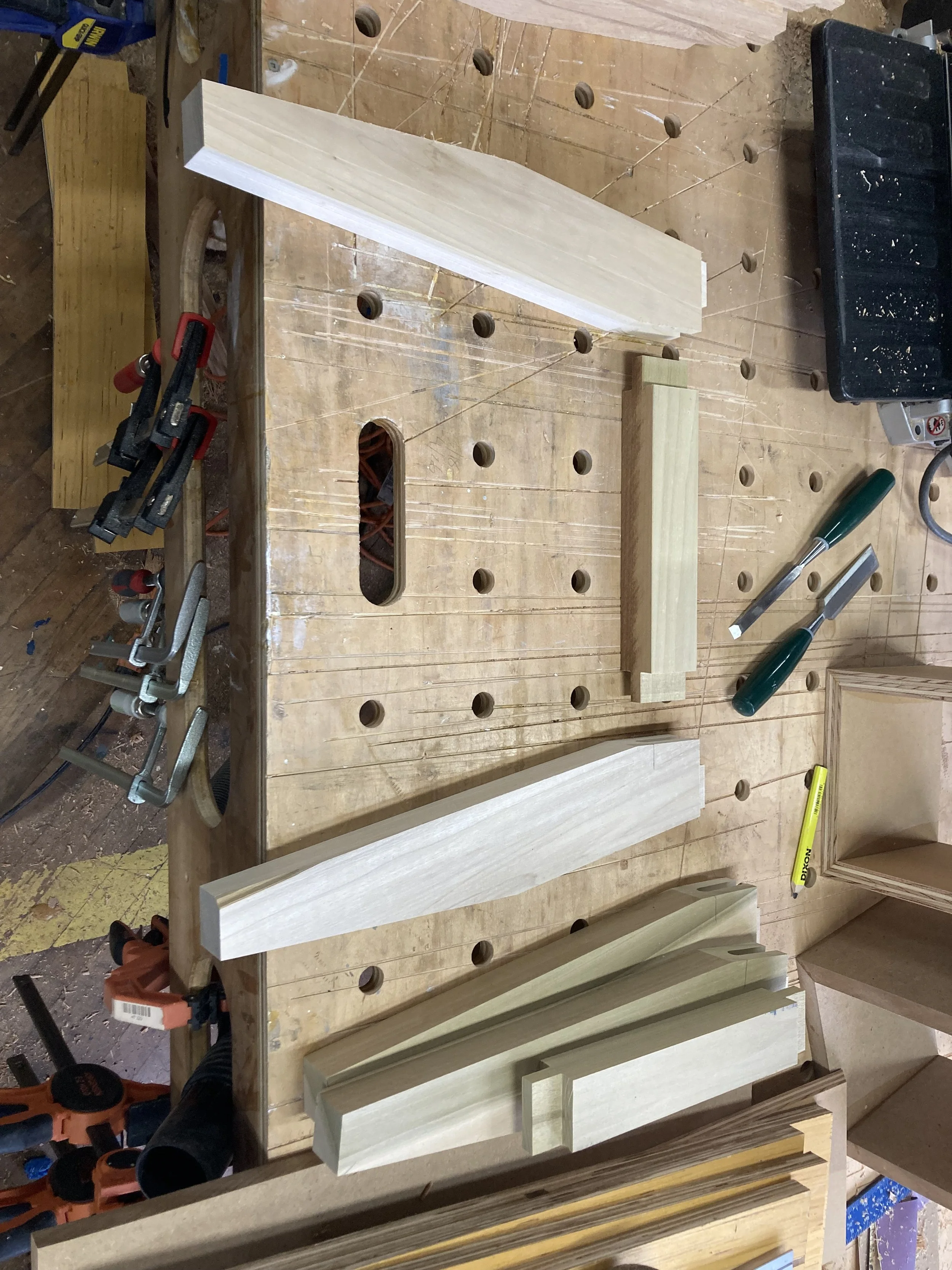 Woodworking workshop scene with a wooden workbench containing clamps, chisels, and several neatly cut wooden pieces.