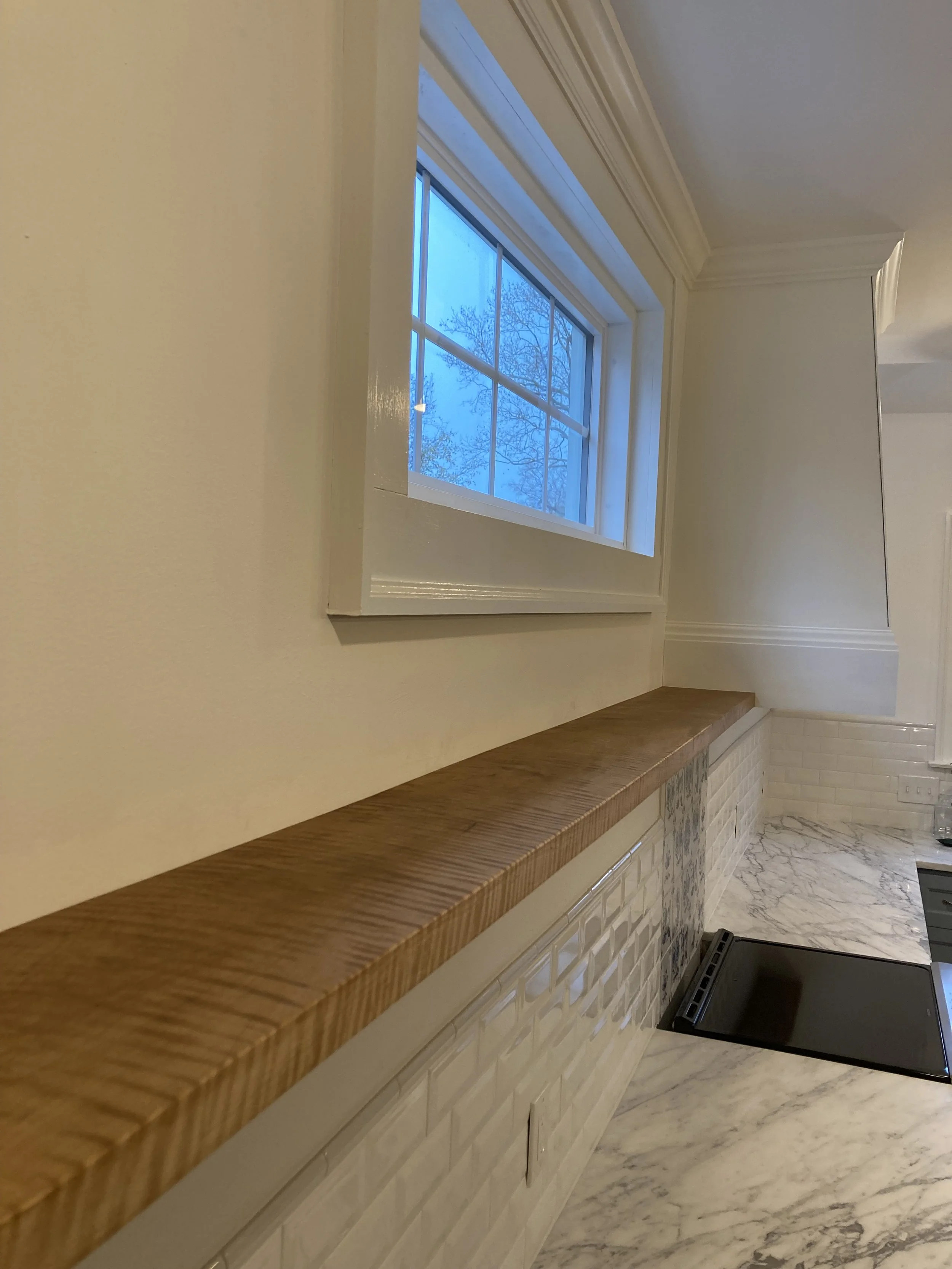 Modern kitchen interior with marble countertop, white subway tile backsplash, wooden shelf, and large window with a view. Elegant and minimalistic design.