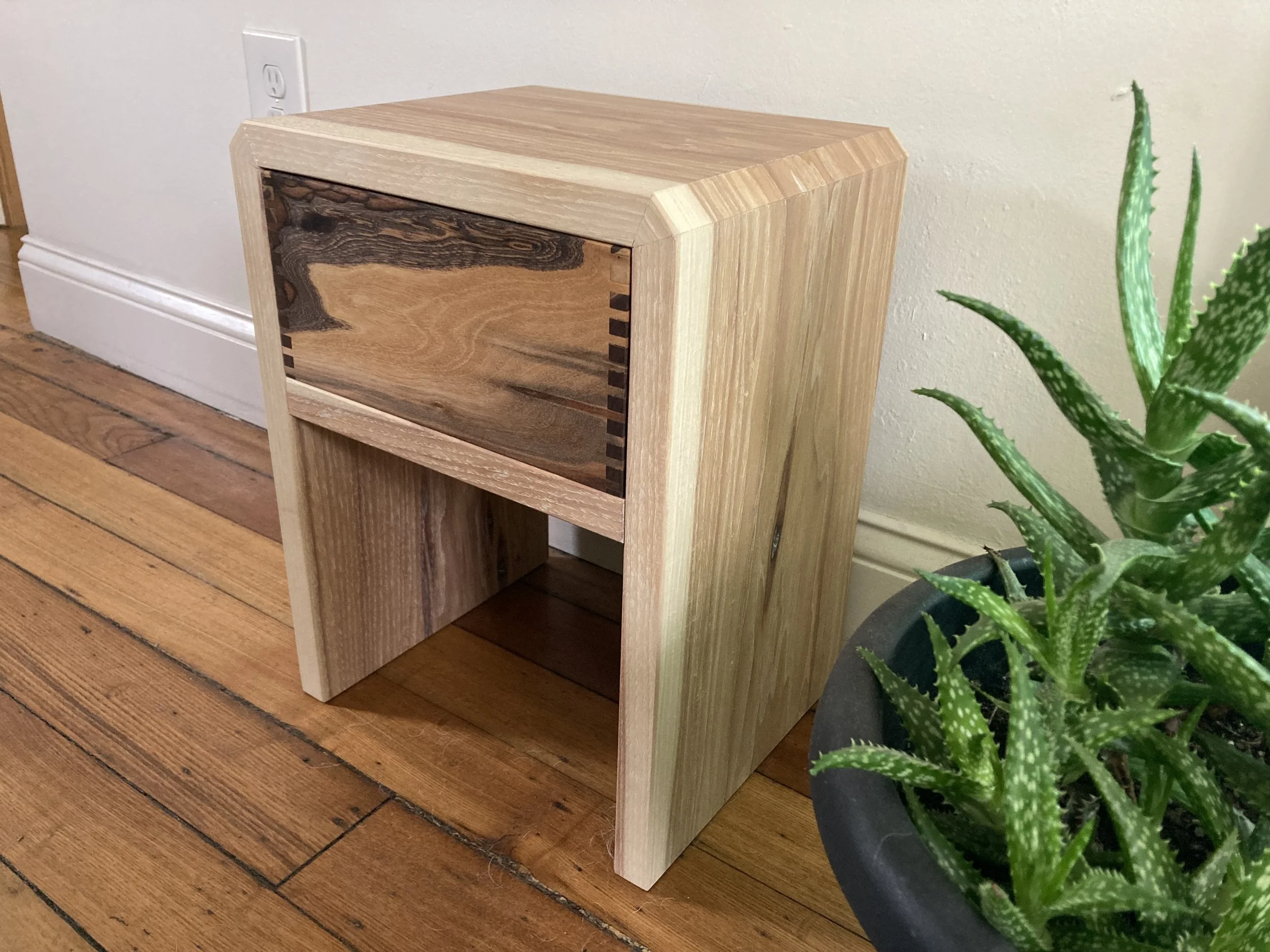 Wooden table with drawer next to potted plant on wooden floor