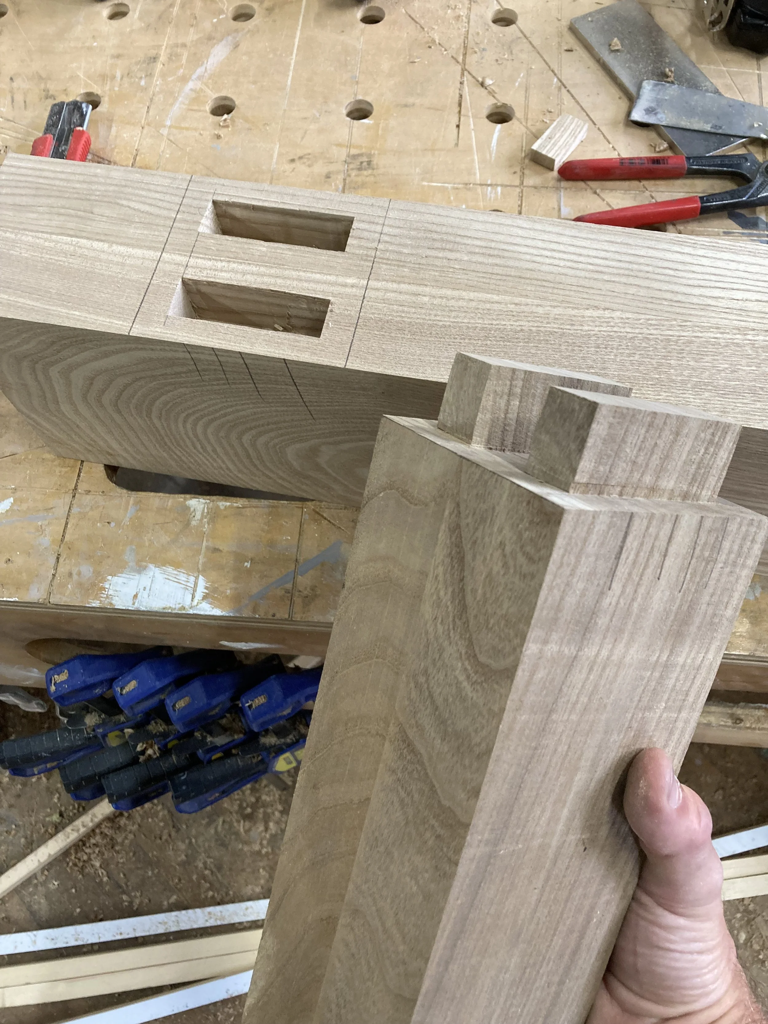 Wooden pieces with mortise and tenon joints on a workbench with tools.