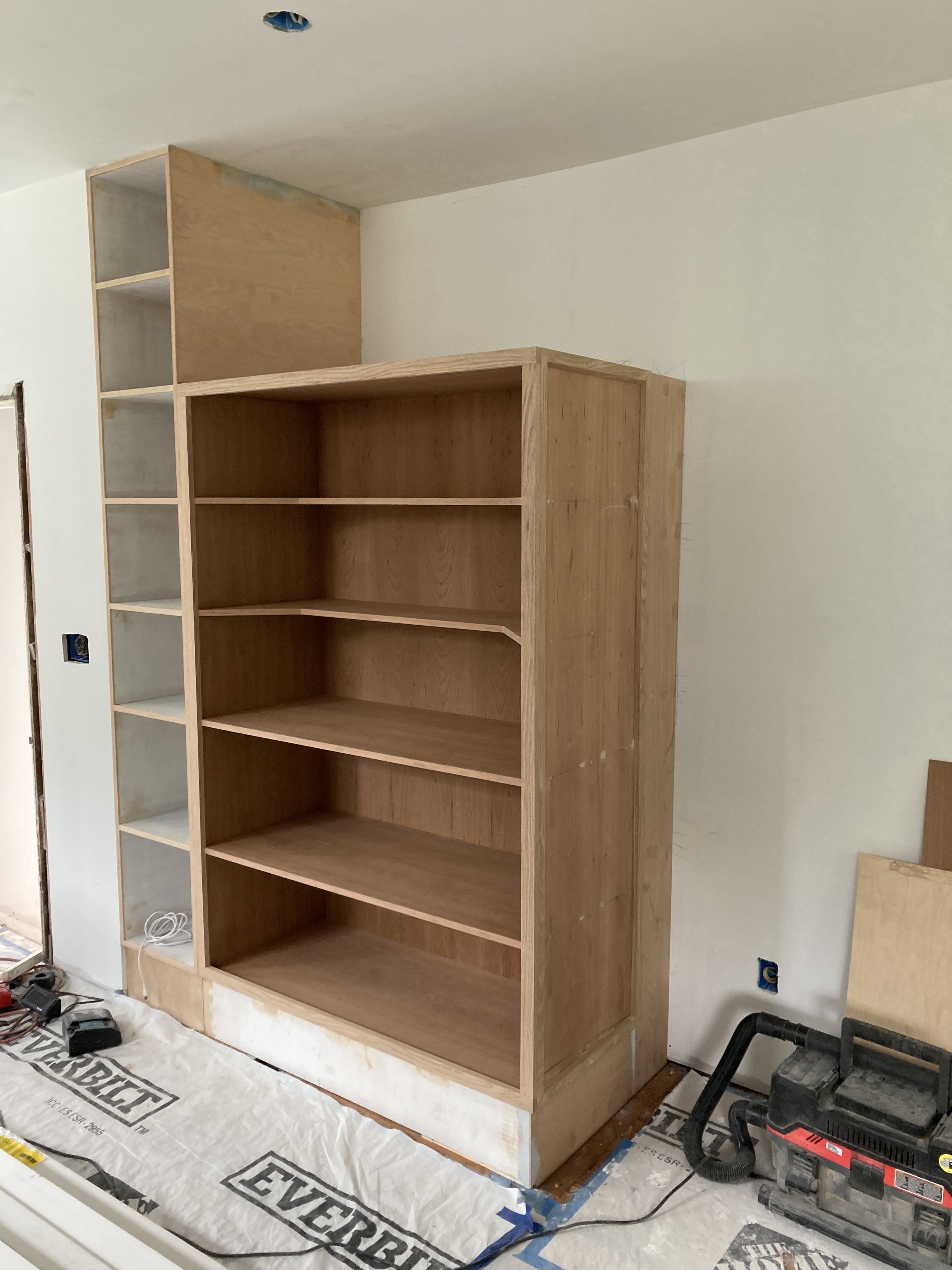 Unfinished room with built-in wooden bookshelves under construction, surrounded by tools and materials on the floor.
