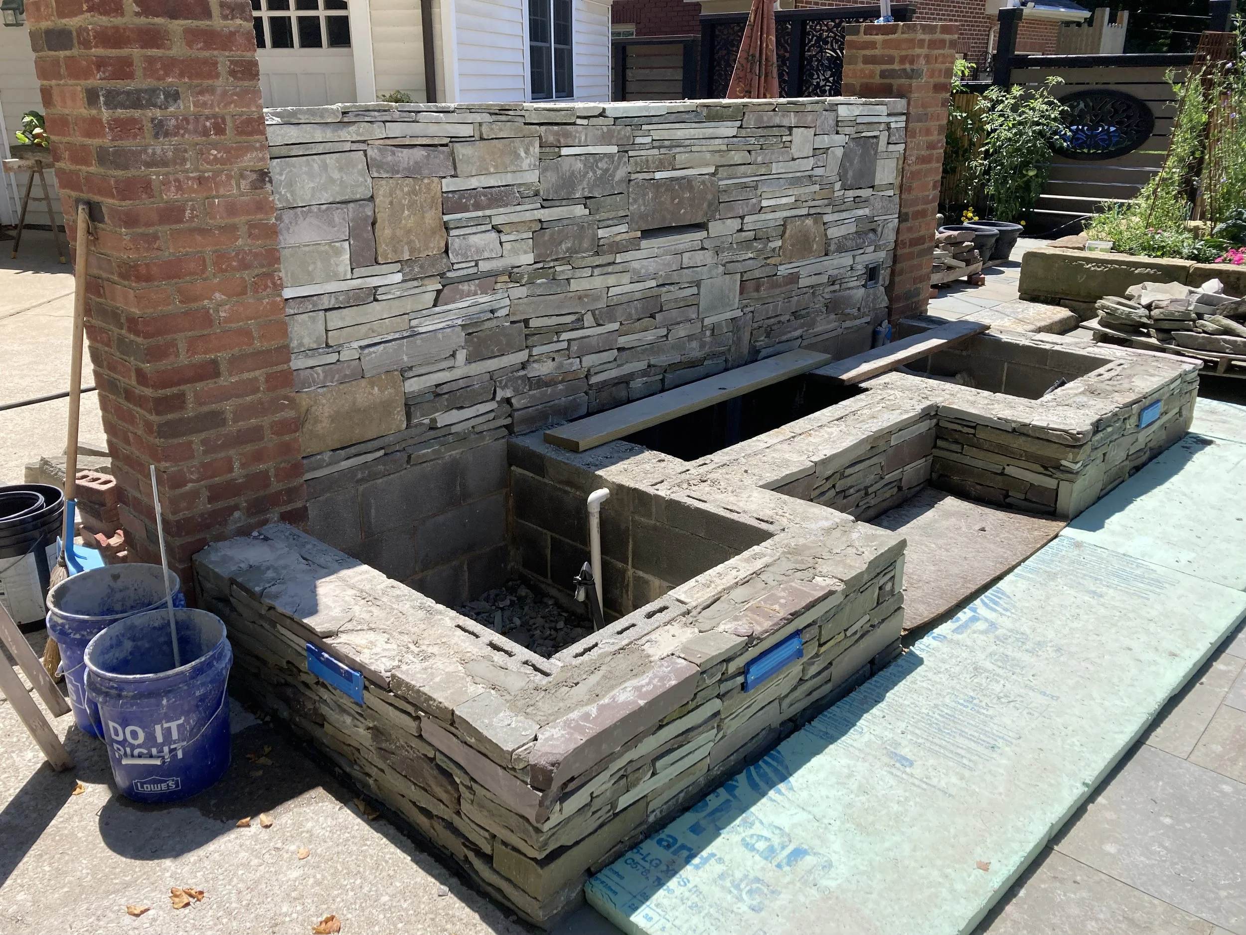 Outdoor stone barbecue construction with brick and stone walls, work in progress, tools on the side.