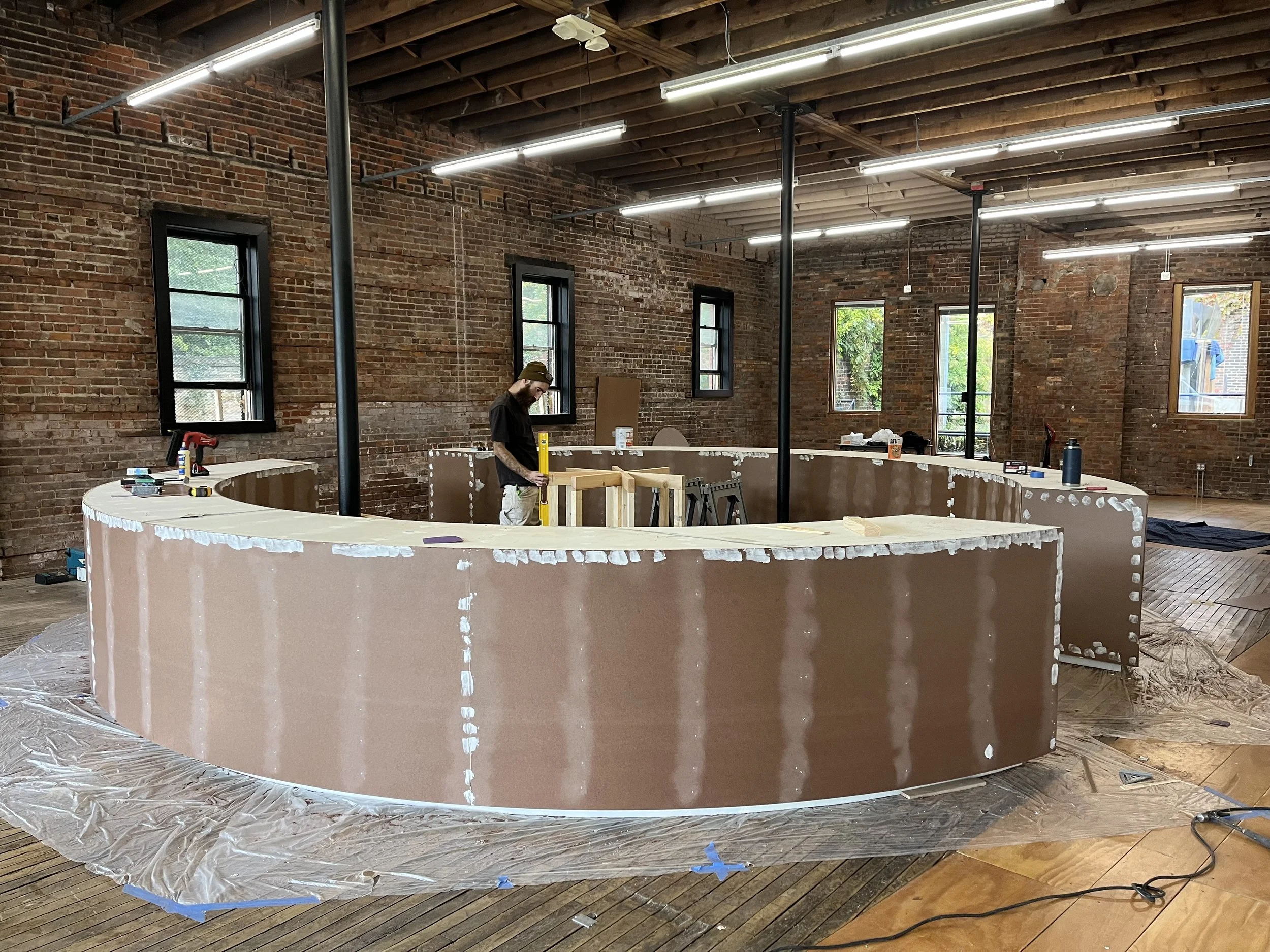 A person working on a circular structure under construction inside a room with exposed brick walls and wooden flooring.