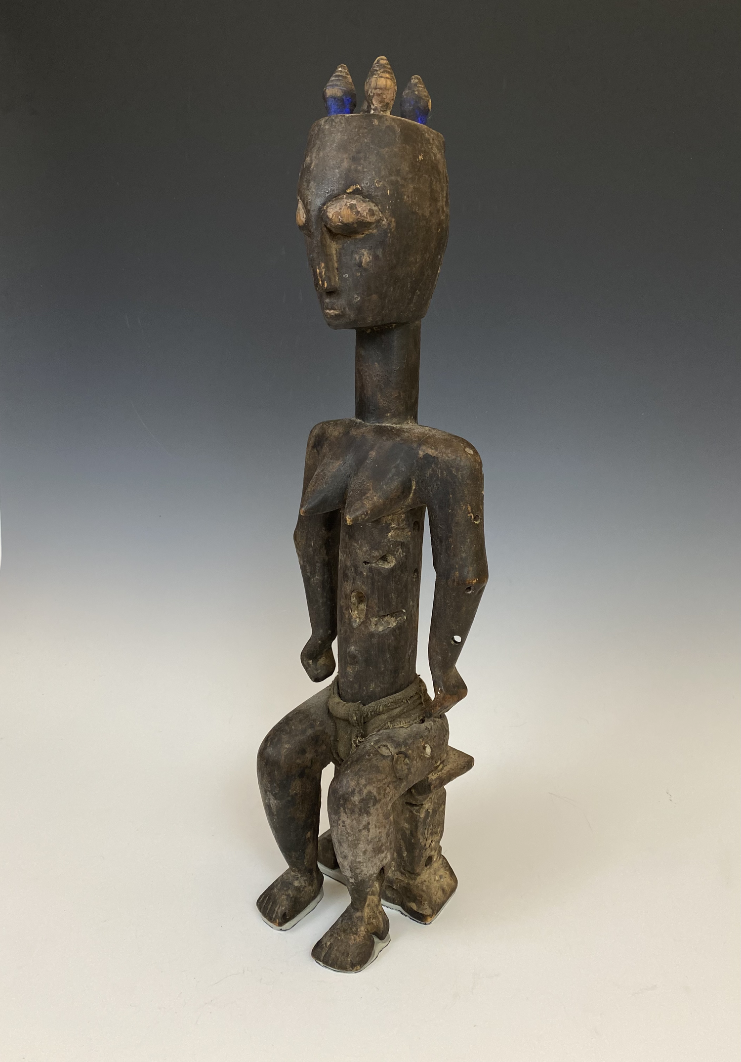 Ebrié (Lagoons people) female figure (Nkpasopi) seated on a stool, Côte d’Ivoire. Wood, pigment, fabric. 25” H. Estate of Thomas McNemar (1931-2020). McNemar lived and collected throughout Central and West Africa in the 1960s and 70s. He established