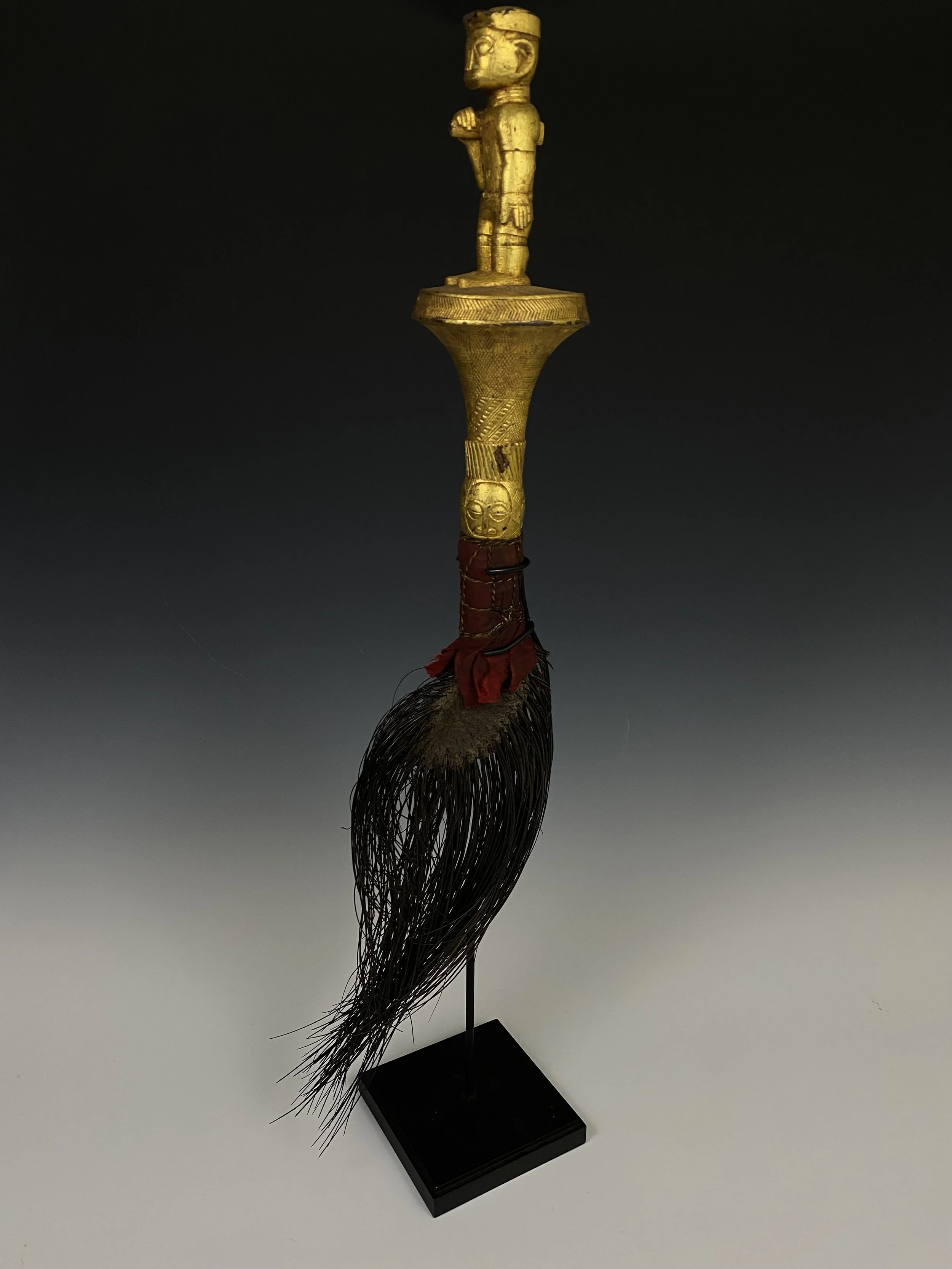 A fly whisk made of an elephant tail is known as “mena”. Wood, covered with gold foil, elephant tail/ hair, textile. H 70 cm. “At one time elephant tail fly whisks (mena) were ubiquitious in the courts of many Akan chiefs. At the Asante Odwira festiv