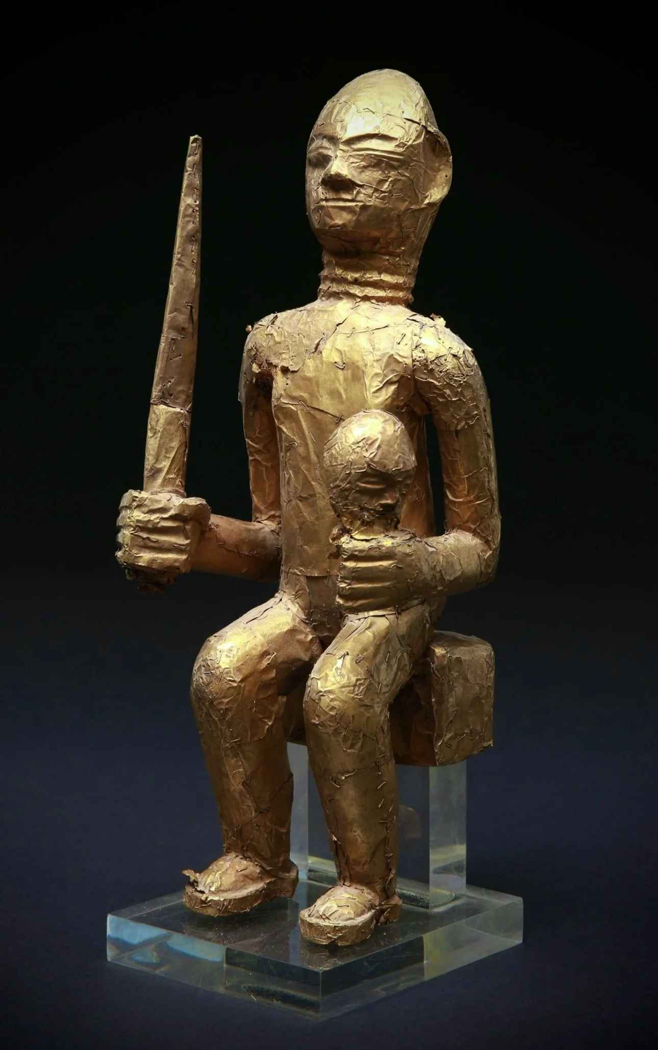 An Asante Linguist staff finial, "Okyeame Poma”. Wood, covered with gold foil attached to the wood with gold staples. H 27.5 cm.  Depicted here is an executioner displaying an executioner's sword and a severed head.  The image can also represent the 