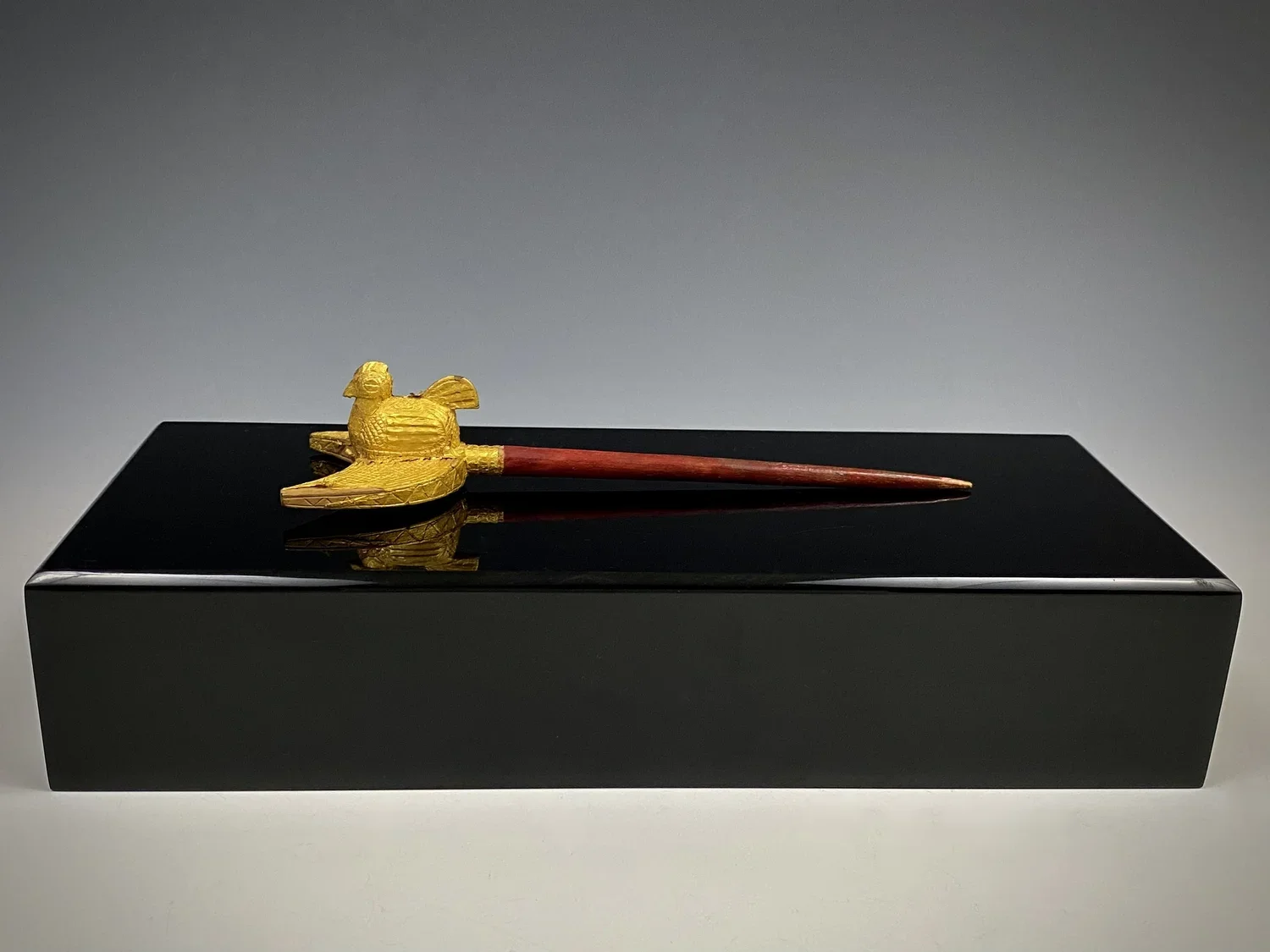A Baule (Baoulé) hair pin ornament with the image of a hen on a crescent (moon). Wood covered with gold foil, 16.5 cm. In Baoulé art, the hen image often represents fertility, motherhood, and nurturing. The hen is revered as a symbol of fertility bec