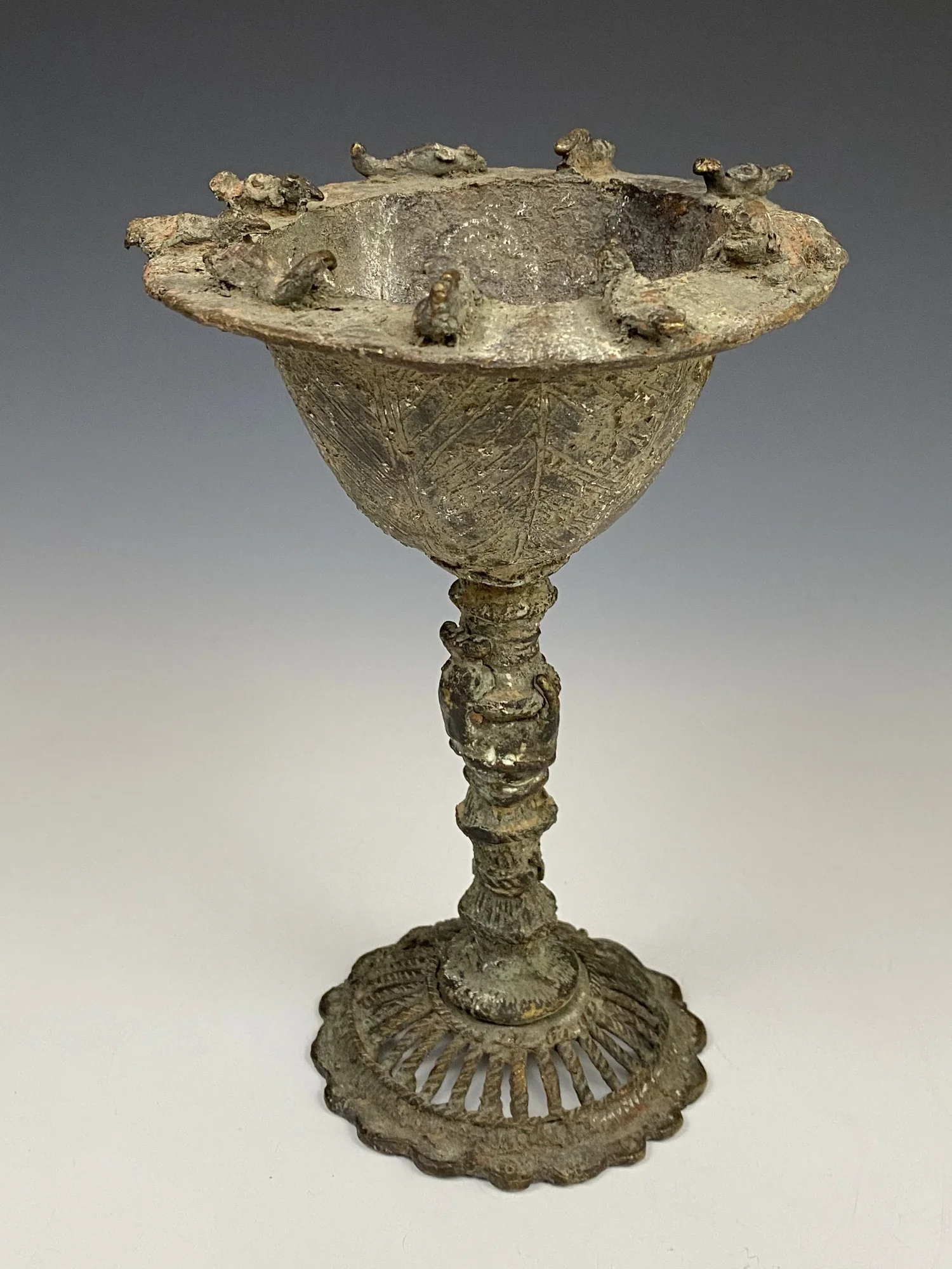 Asante oil lamp. Cast bronze. The animals depicted on the edge of the shell (among other things 6 birds) refer to proverbs such as "Birds of the same species drink from the same pond". The stem takes the form of the segmented cane babadua also seen i