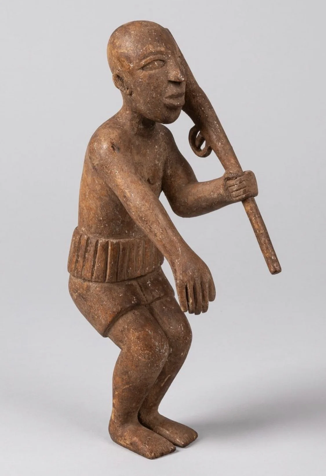 Asante prestige figure or remnant of an “Okyeame Poma” staff finial. The figure is in two parts consisting of a male figure and a rifle. The figure has his right hand out, palm facing downward. The left arm holds a rifle. Wood. H: 27 cm, H: 10,6 inc