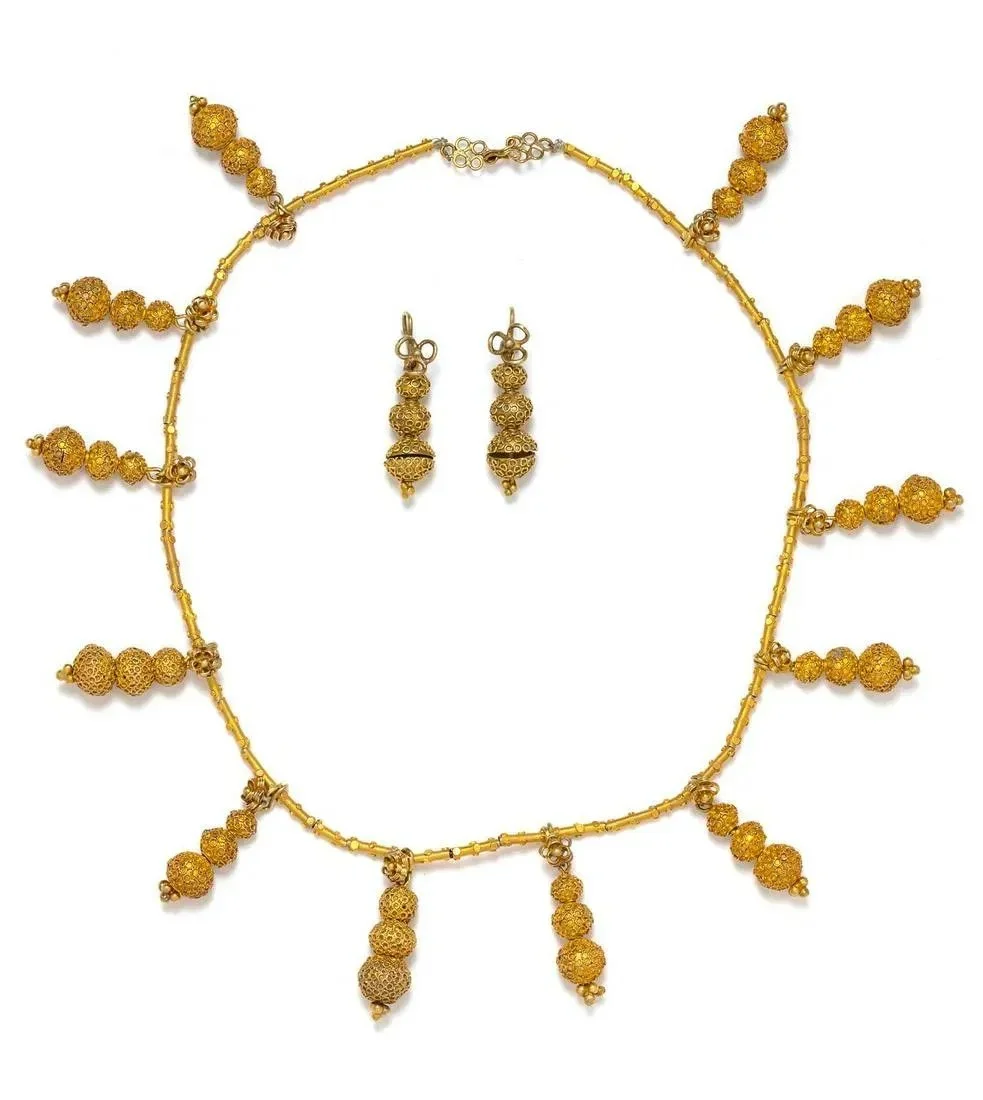 An Akan (Côte d’Ivoire/Ghana) gold/silver alloy demi-parure. This design was influenced by Victorian fashion. It consists of a necklace strung with numerous tubular beads and suspended triple spherical bead pendants, together with a matching pair of