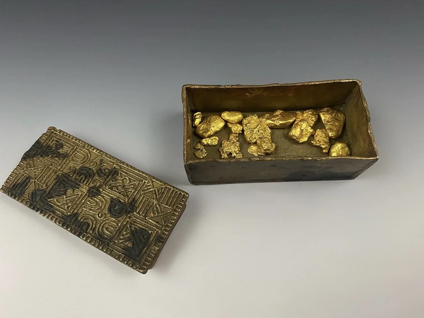 Asante gold dust box, "adaka" with an intricately designed lid, Ghana, copper alloy. H 2.5cm. W 6.5cm. (Displayed with natural gold nuggets from various locations.) Published: Lüthi, Werner & David, Jean (2009). Exhibition catalogue: Helvetic Gold Mu