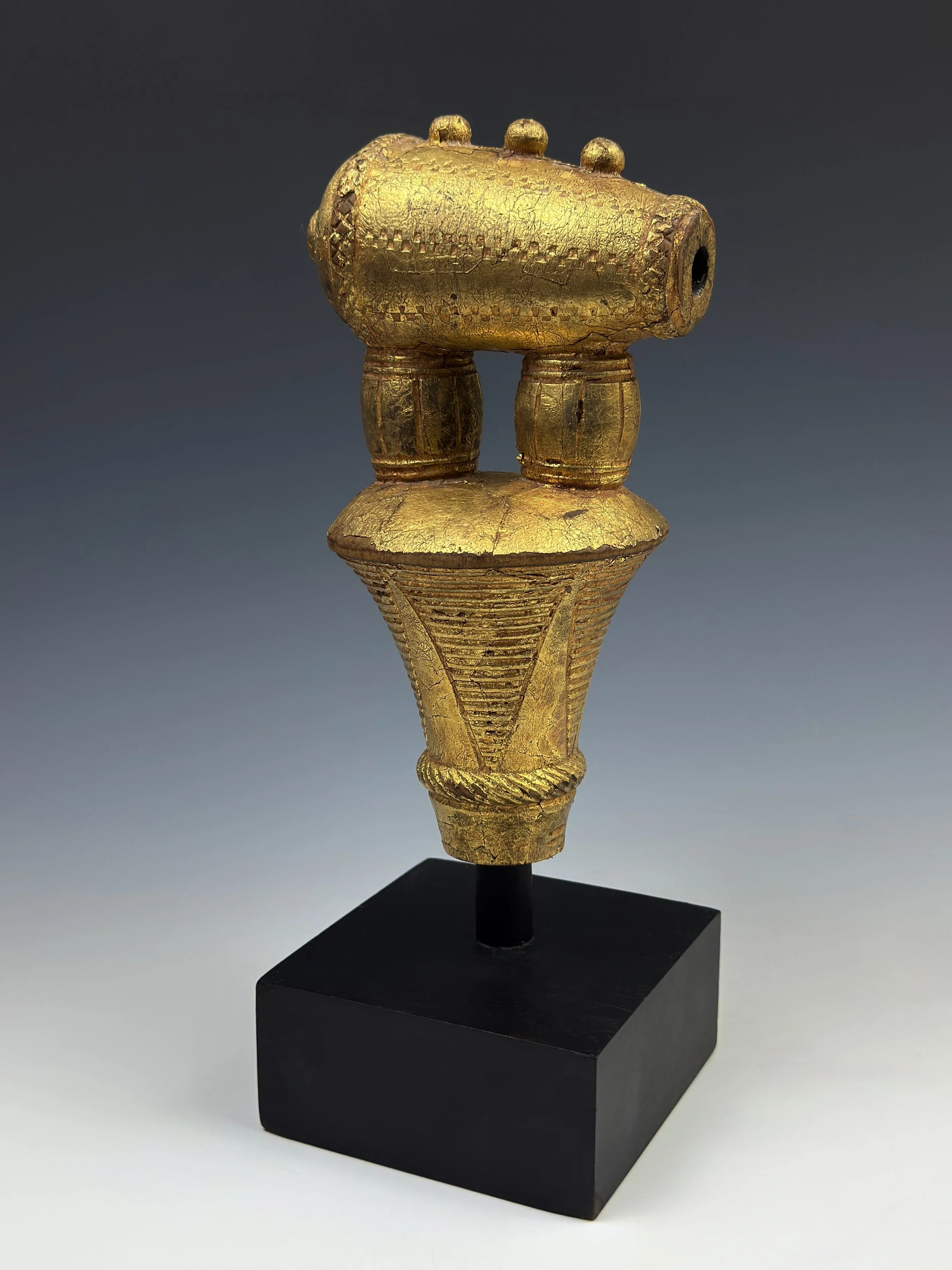 An Akuapem counselor’s staff finial (okyeame poma). Imagery of cannons and powder kegs speaks to the readiness, strength, and power of the state and chief. The imagery also appears to depict 3 cannon balls on the top of the cannon. This example carve