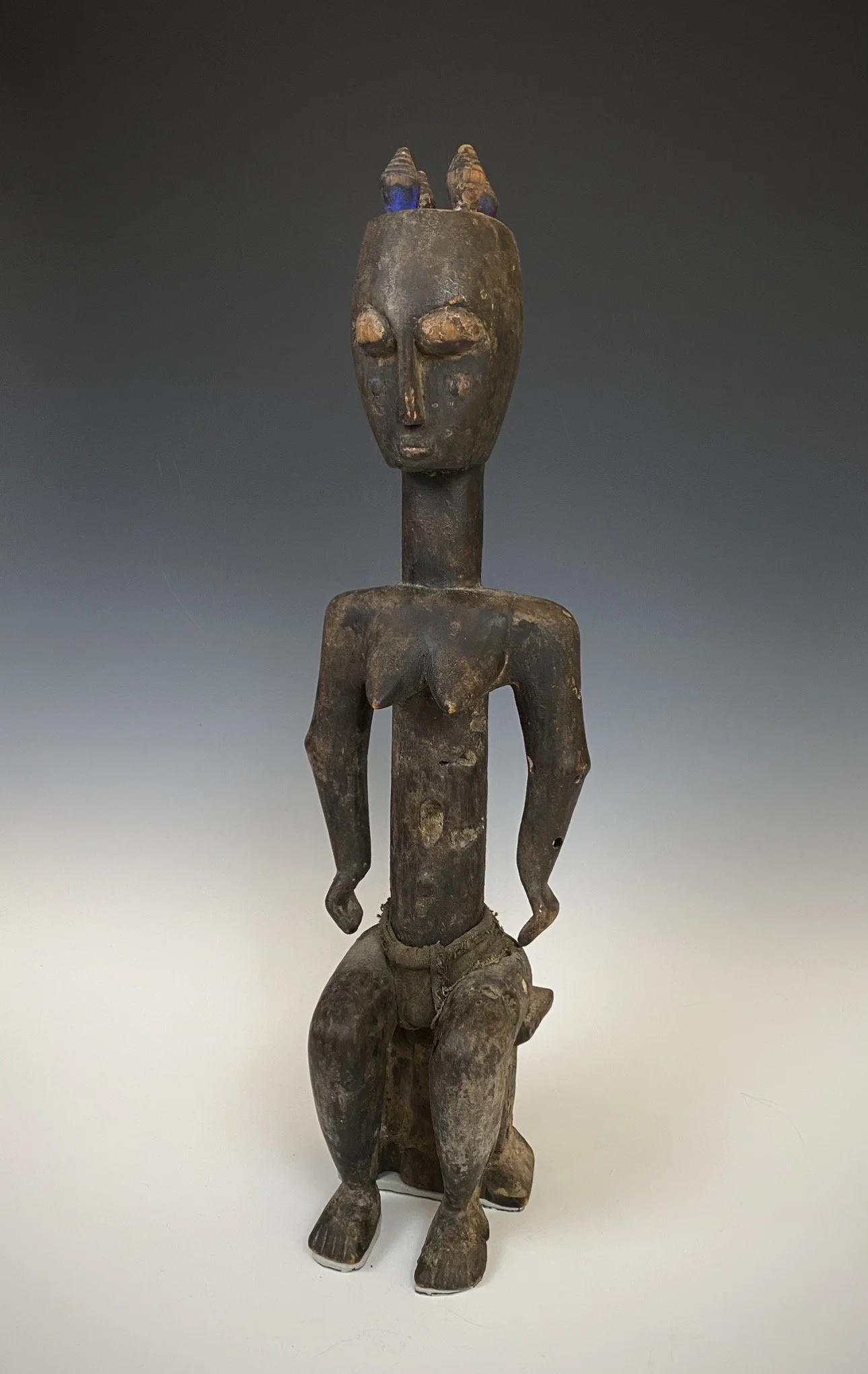 Ebrié (Lagoons people) female figure (Nkpasopi) seated on a stool, Côte d’Ivoire. Wood, pigment, fabric. 25” H. Estate of Thomas McNemar (1931-2020). McNemar lived and collected throughout Central and West Africa in the 1960s and 70s. He established 