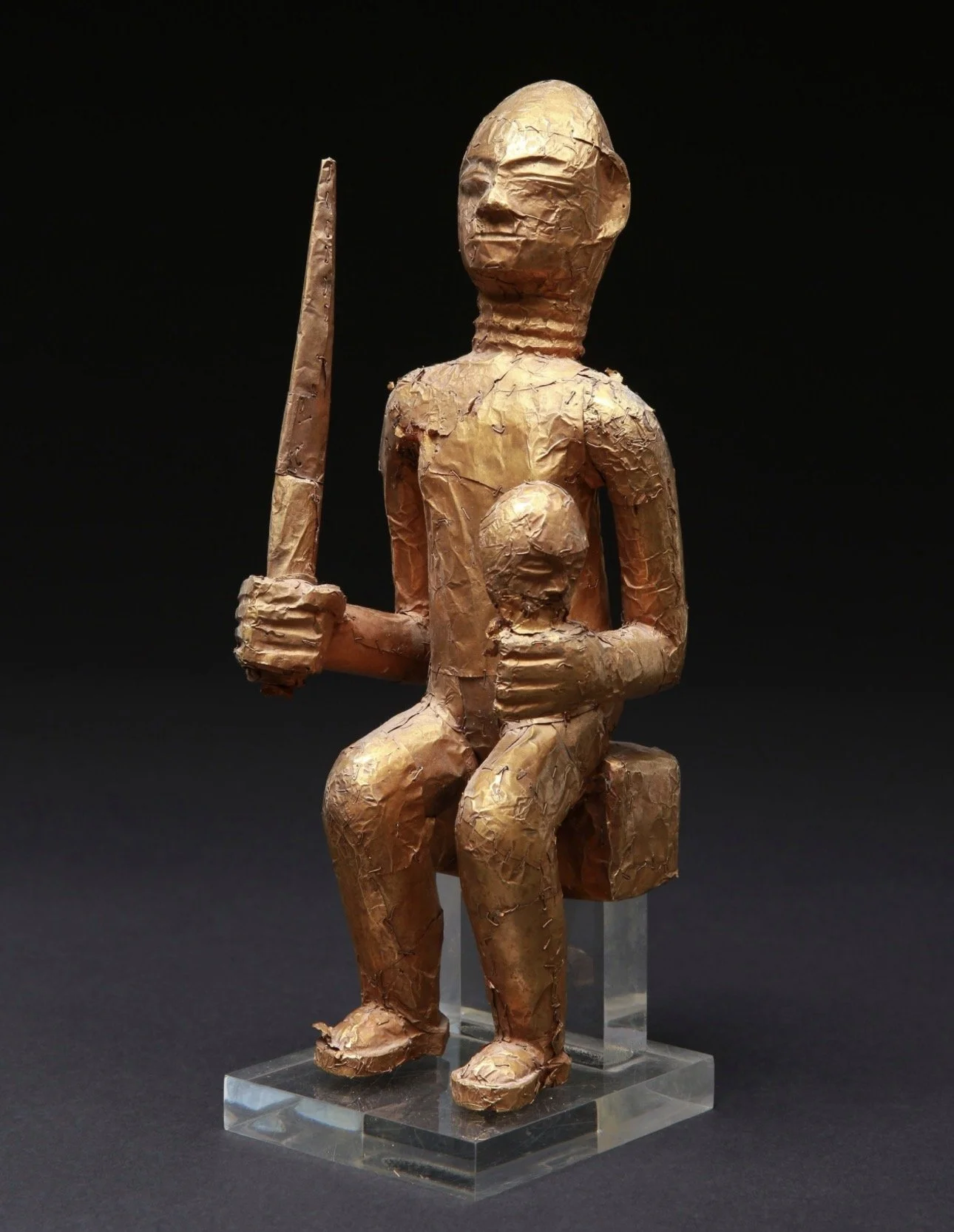  An Asante Linguist staff finial, "Okyeame Poma”. Wood, covered with gold foil attached to the wood with gold staples. H 27.5 cm.  Depicted here is an executioner displaying an executioner's sword and a severed head.  The image can also represent the