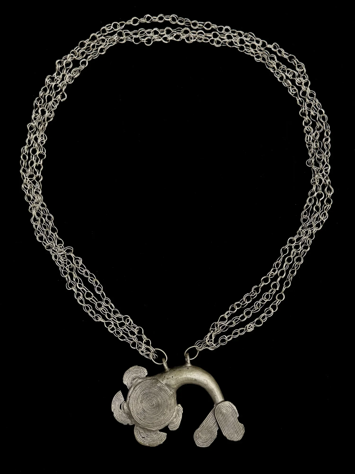 Akan three-stranded chain with mudfish pendant. Silver alloy. Associated proverb: "When the mudfish swallows anything, it does so for its master" (crocodile) that is, what is good for his subjects is good for the chief". Provenance: Zemanek-Münster,