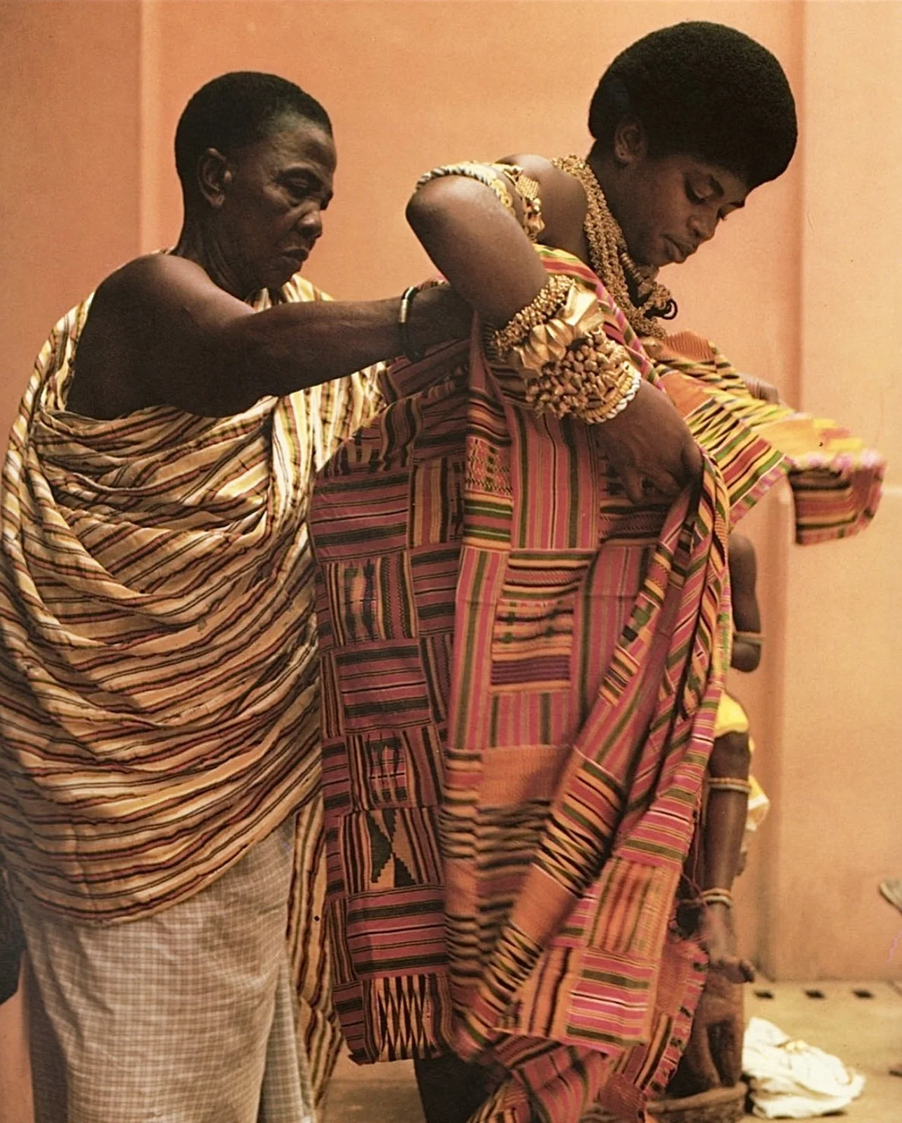 Two woman preparing for a ceremony adorned with gold regalia and women's kente. ca. 1997.  Photo credit: Fabby Nielsen