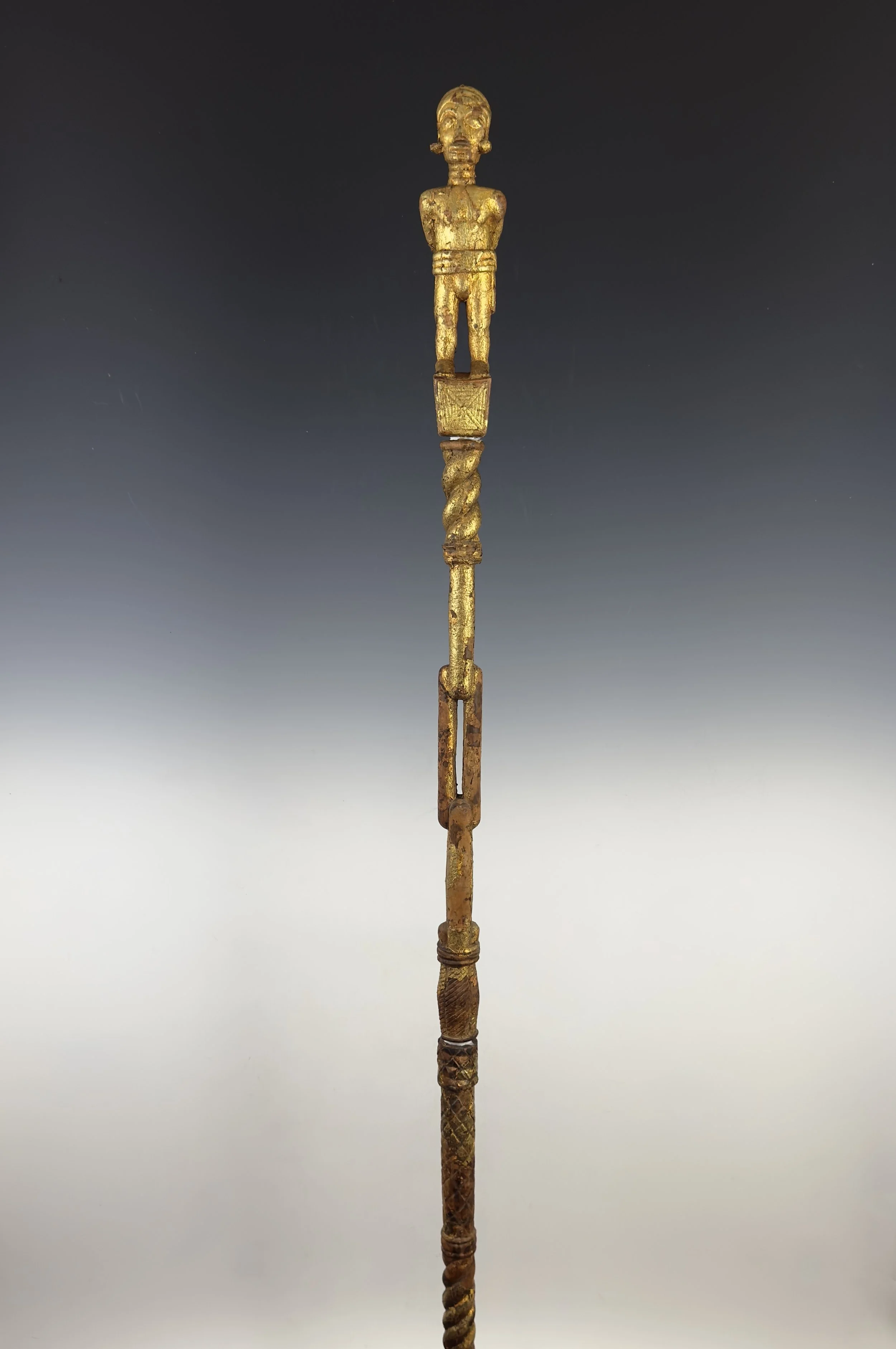 An Akan counselor’s staff (okyeame poma), carved wood covered with gold leaf. Ghana.  The staff is in three sections consisting of the finial on top, and two lower segmented staff sections. Michelle Gilbert describes the staff as “Showing a prisoner